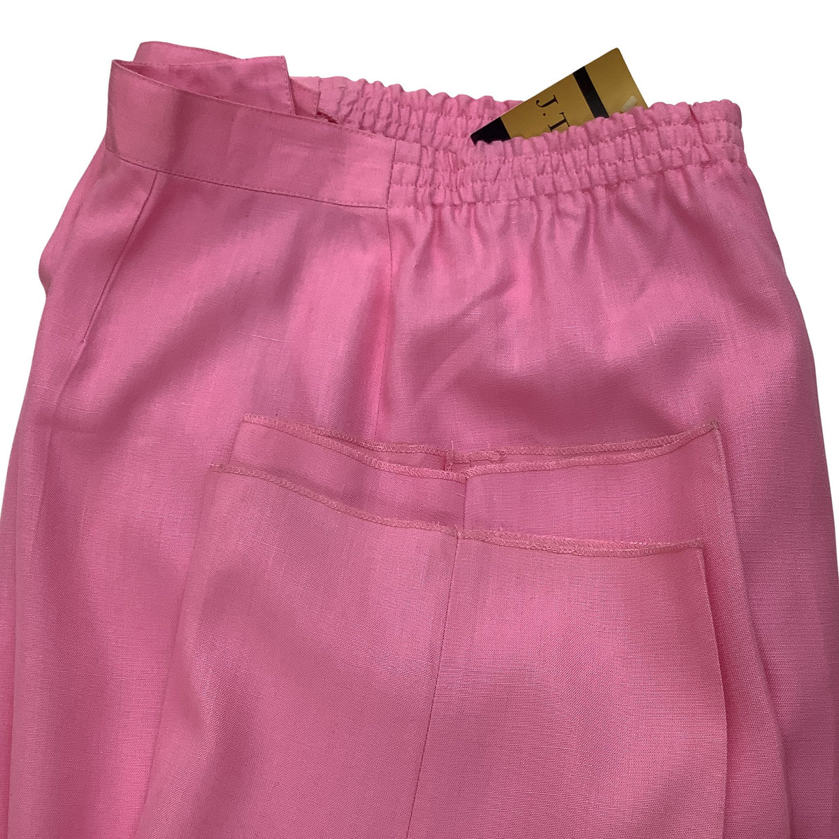 Pink trousers with an elastic waistband and un-hemmed pant leg shown folded on a white background with a gold and black tag visible inside the waistband.