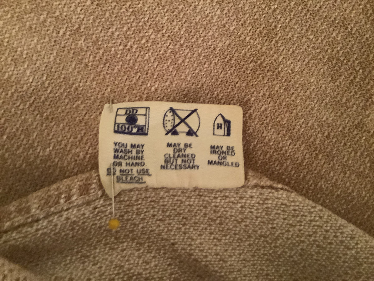 A close-up of a Bates vintage 1950s fabric label with black laundry care symbols and text, attached to a piece of beige textile.