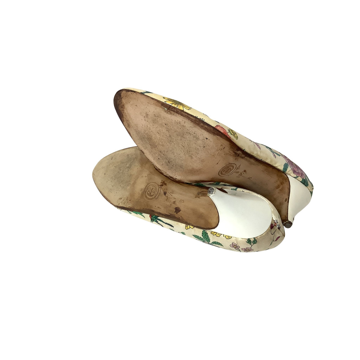 A pair of vintage floral slip-on shoes shown from the side, revealing a cream-colored fabric upper with a multicolor floral pattern and heavily worn, stained brown soles.
