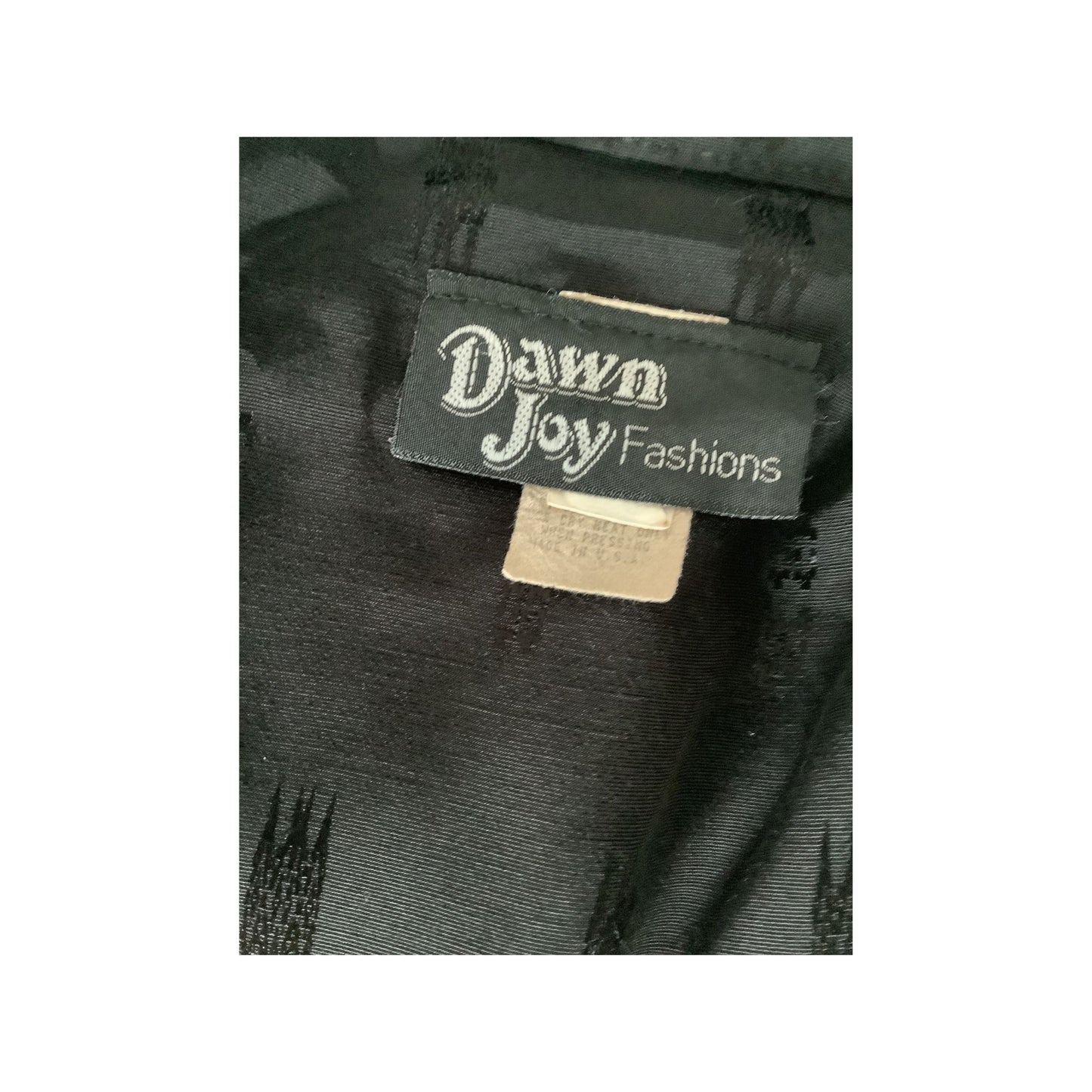 Close-up of a black garment label reading 'Dawn Joy Fashions' on dark textured fabric.
