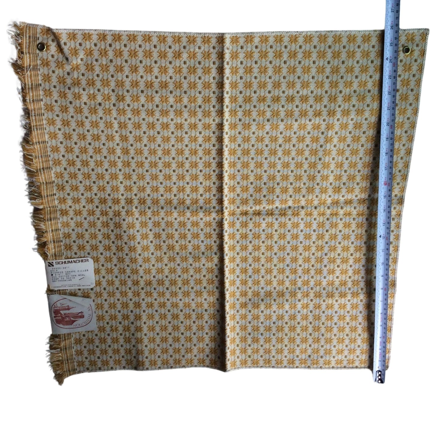 1950s Schumacher wool fabric with a repeating geometric pattern in yellow, brown, and white, featuring fringed edges and a size measurement ruler standing alongside it on a white background.