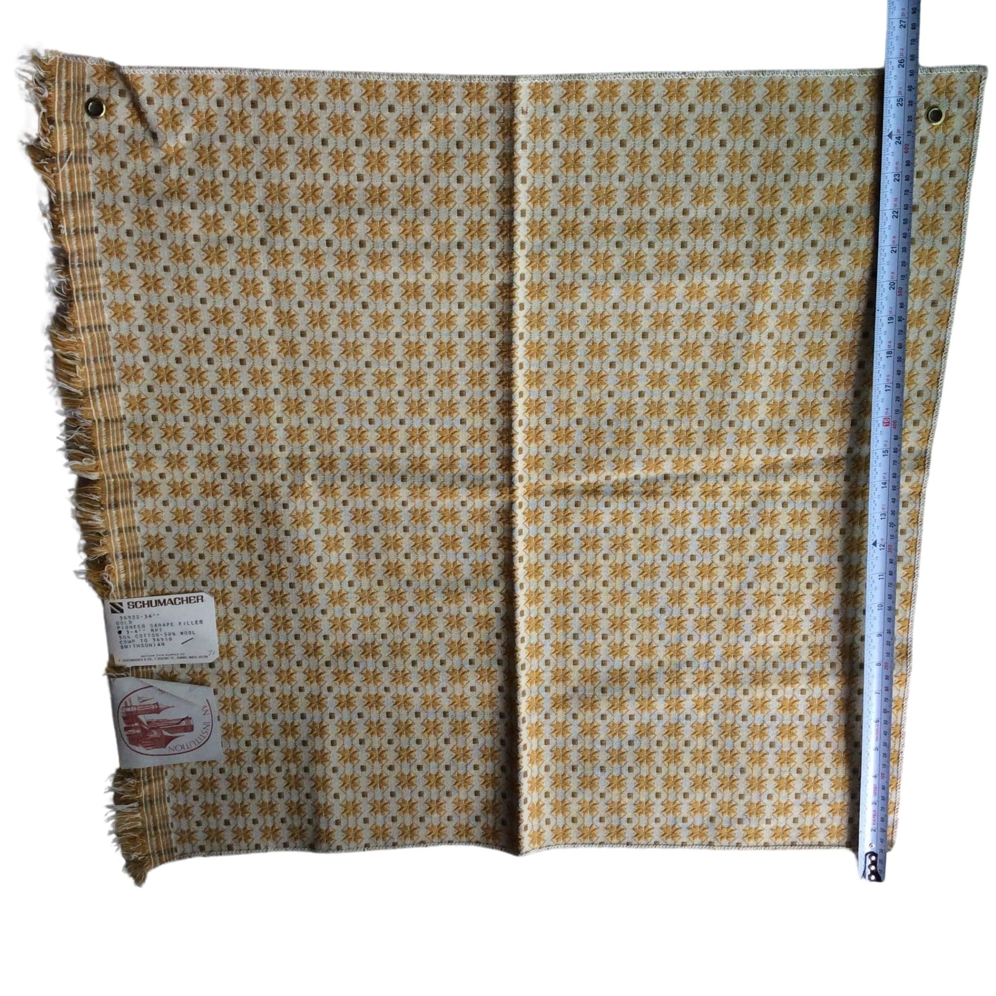 1950s Schumacher wool fabric with a repeating geometric pattern in yellow, brown, and white, featuring fringed edges and a size measurement ruler standing alongside it on a white background.