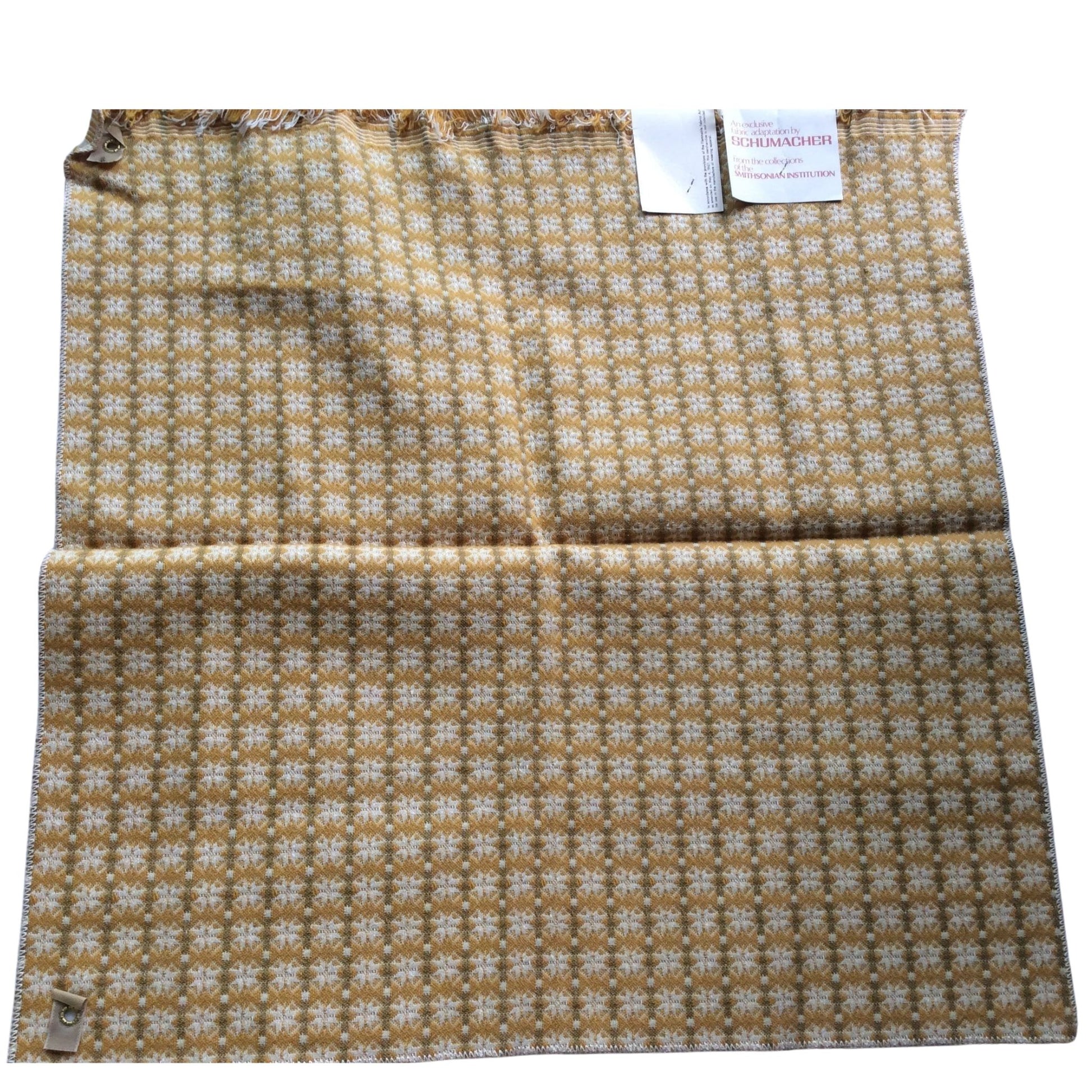 1950s Schumacher wool fabric with a repeating white floral pattern on a warm brown background, featuring a small metal tag and a white paper brand tag.