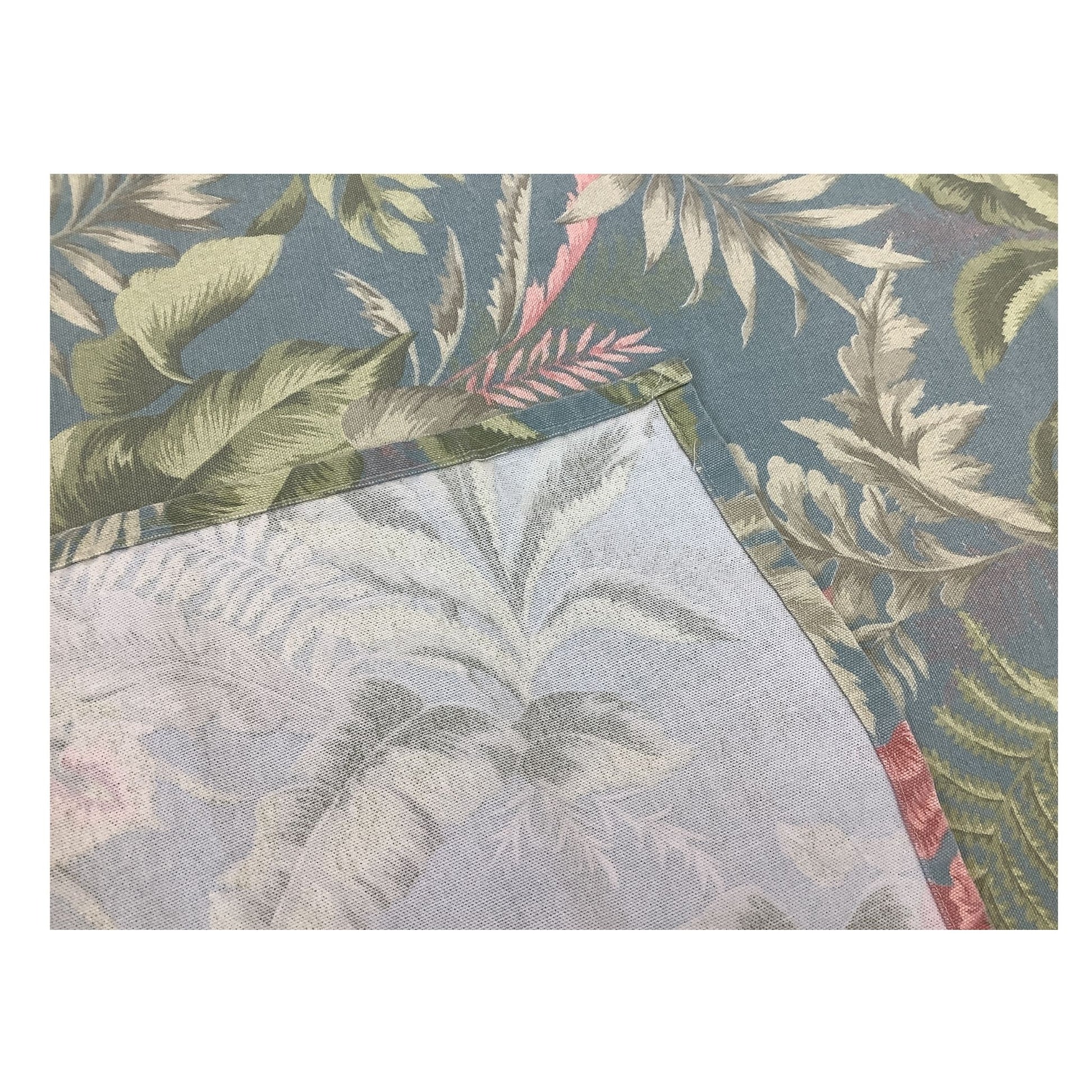 A close-up machine stitching of a tropical leaf patterned tablecloth, showing a dusty blue, green background with white and pink botanical motifs, with a folded section revealing a lighter reverse side.