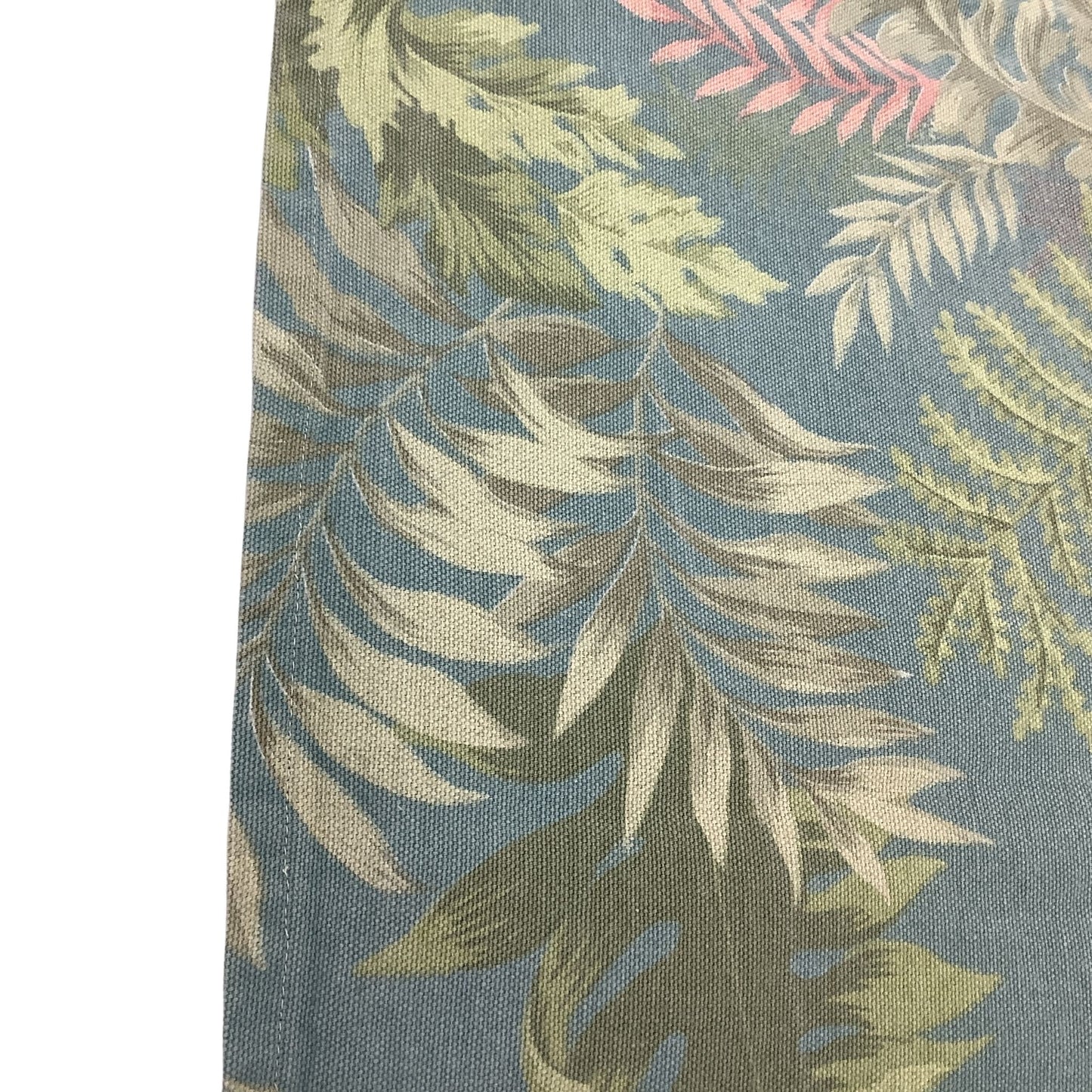 Sitched edge close-up view of a woven fabric with a tropical leaf pattern on a muted blue background, featuring beige, olive green, and soft pink leaves.