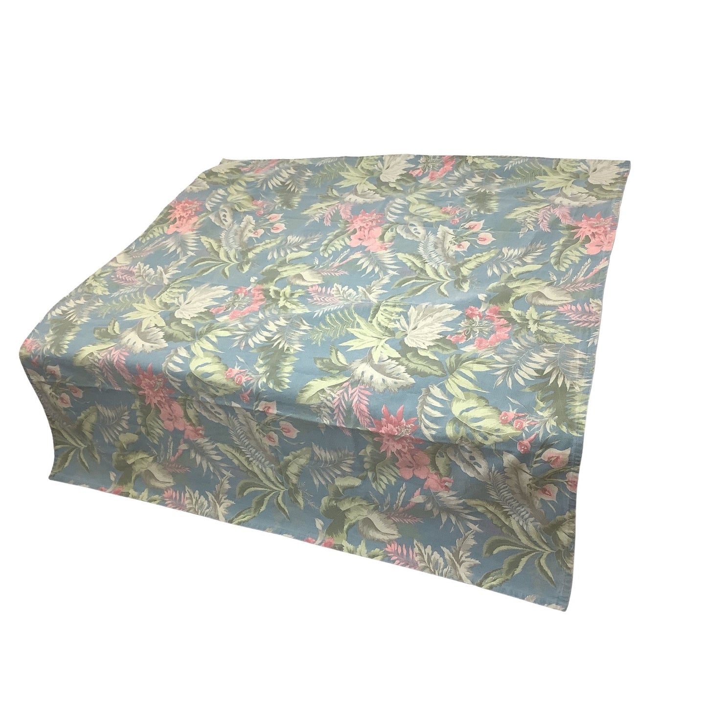 Side-view of a square tablecloth with a tropical leaf and floral pattern in shades of blue, green, and pink, shown on a plain white background.