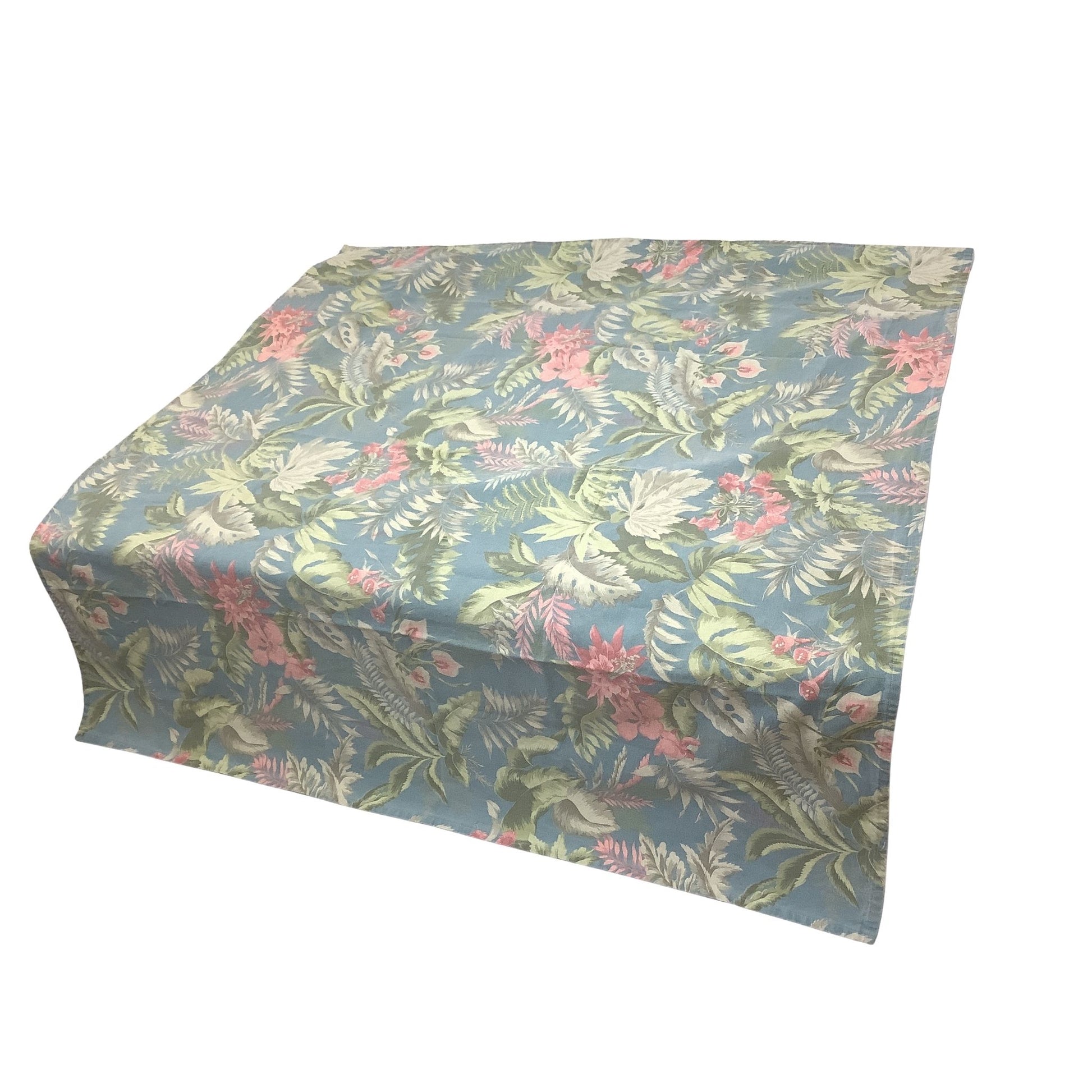 Side-view of a square tablecloth with a tropical leaf and floral pattern in shades of blue, green, and pink, shown on a plain white background.
