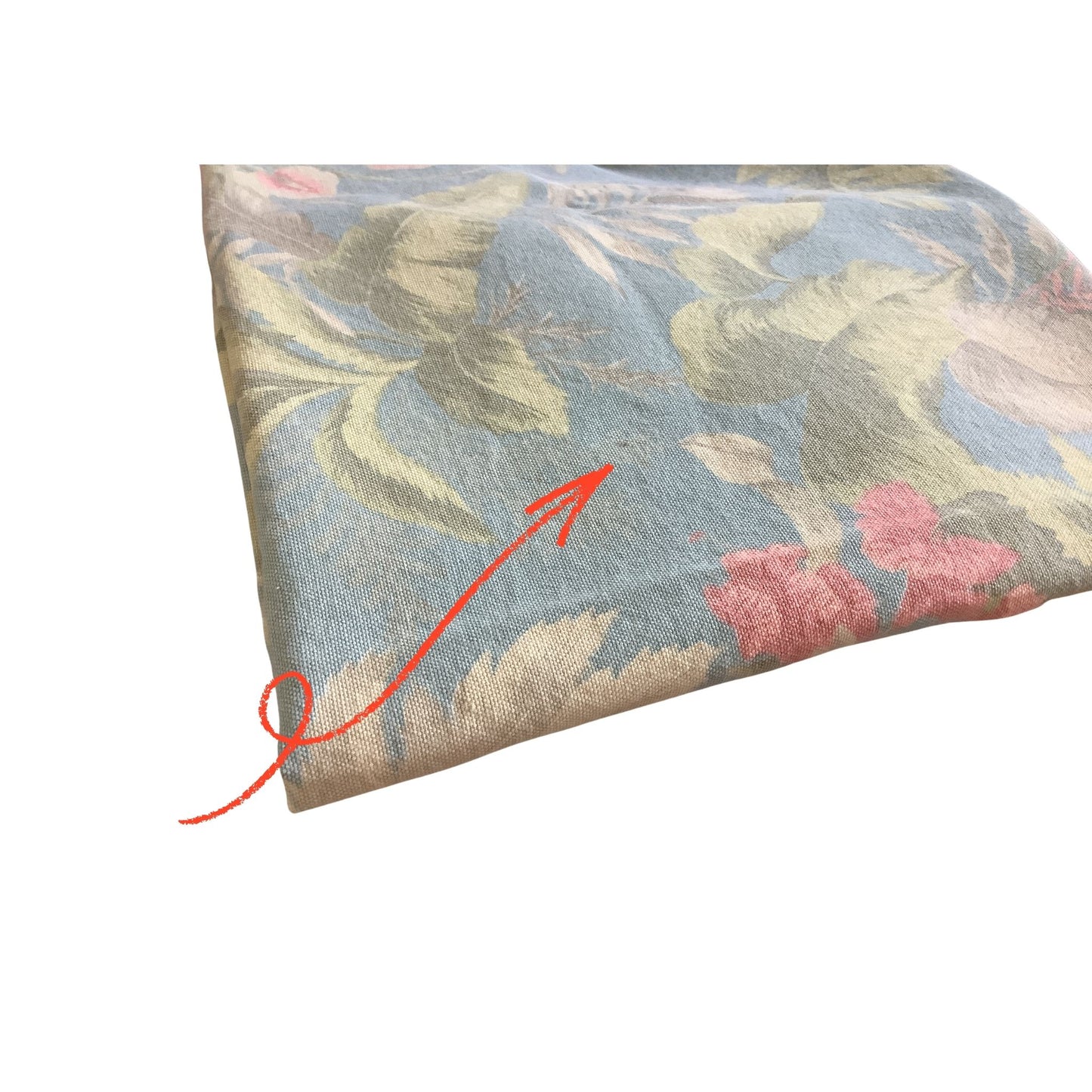 folded art noveau folded tablecloth with a vintage floral pattern in muted blue, sage green, white, and pink, shown on a plain white background with a red arrow pointing to dark speck.