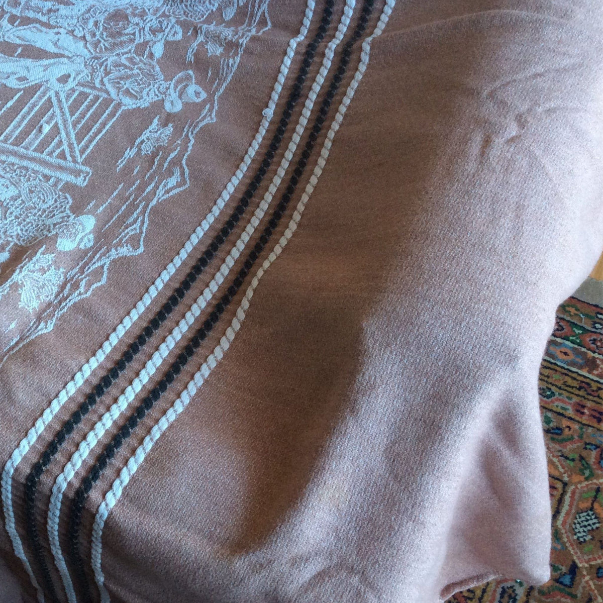 A close-up of a Bates bedspread with white embroidered western motif and two vertical stripes featuring black, white.