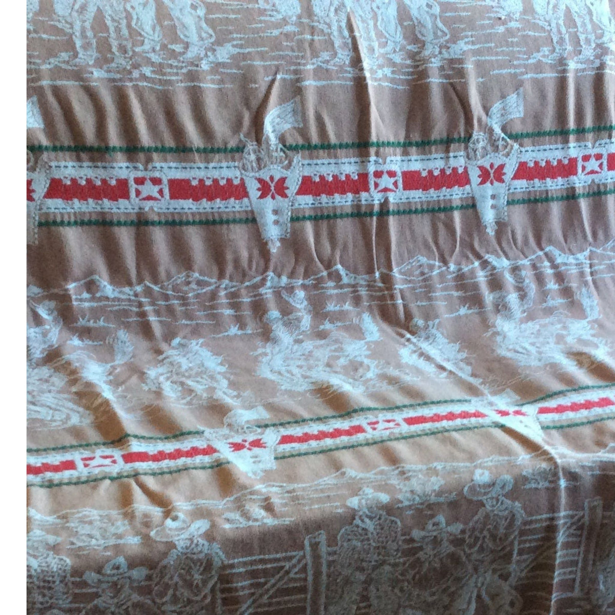 A close-up of a vintage  Bates bedspread with a white embroidered cowboy and landscape pattern, accented by horizontal red and green decorative stripes.