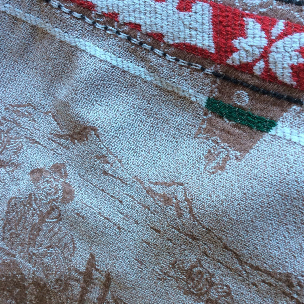 Backside view of Bates vintage bedsprad in a beige base, brown details scenic landscape pattern, a red and white patterned border, and a green accent stripe.