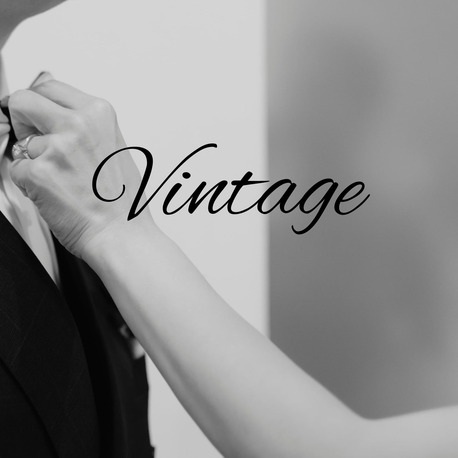 Black and white close-up of a women's arm adjusting a suit jacket, with the word 'Vintage' written in large script across the center.