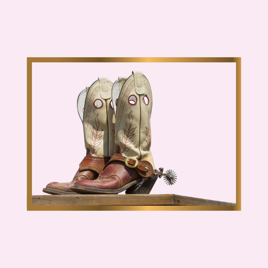 Pair of cowboy boots with decorative elements on a wooden surface against a light pink background.