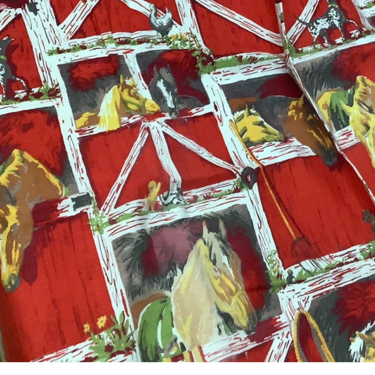 A close-up of vintage western curtains pattern featuring a red barn with white trim and painted horses in yellow, brown, and gray inside the barn stalls.