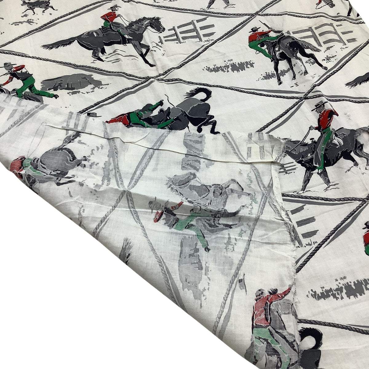 Vintage cowboy fabric in white cotton folded corner with a rustic western print of black horses, riders in red and green, and gray rope details.