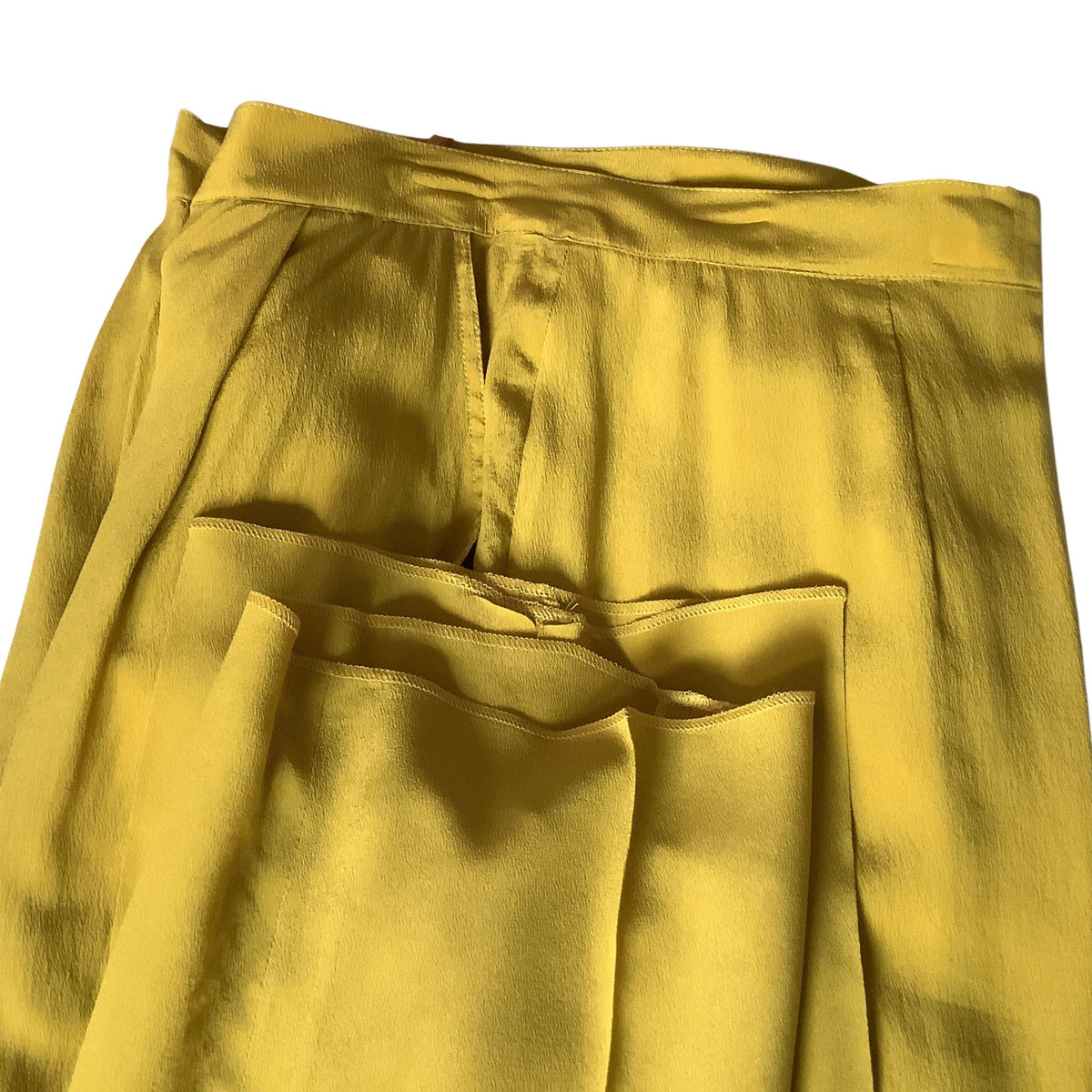 A close-up of a pair of chartreuse green trousers showing the waistband, front crease, and front pockets and unhemmed pant leg.