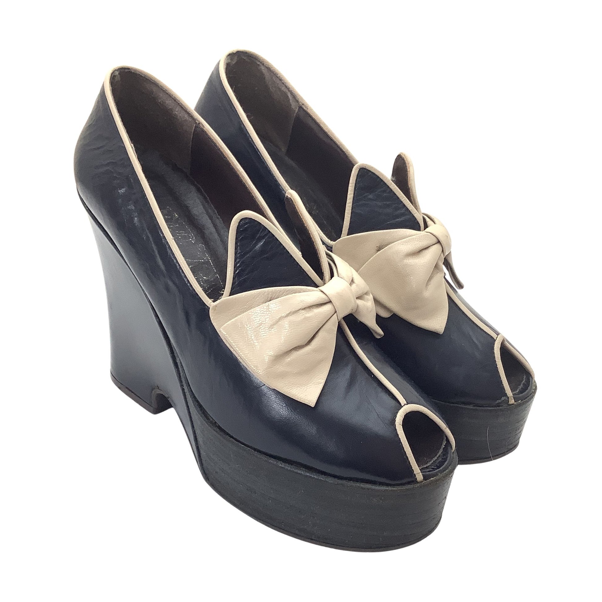 A pair of vintage Elditas platform wedge pumps in navy blue leather with beige leather bows and contrast piping, side view.