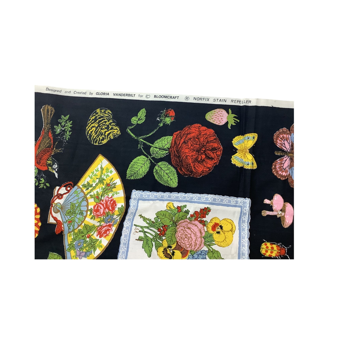 Gloria Vanderbilt vintage patterned fabric featuring a black background with colorful botanical and insect illustrations, including roses, butterflies, a bird, mushrooms, and a floral panel. Printed text 'Designed and Created by Gloria Vanderbilt for Bloomcraft Norfix Stain Repeller'
