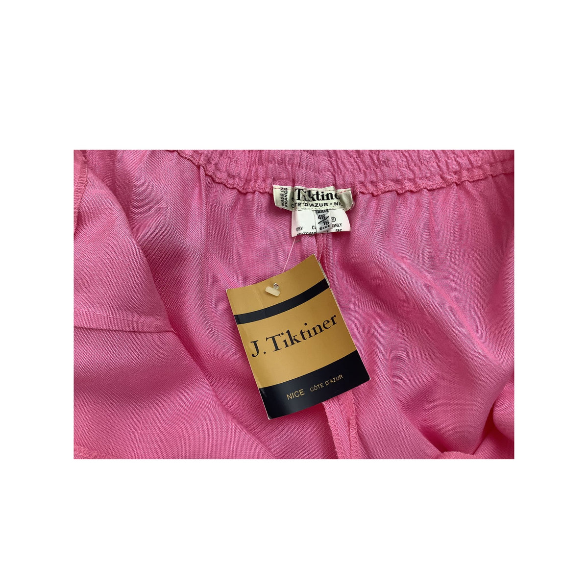 Close-up of a pink garment showing the elastic waistband and a hanging J. Tiktiner paper tag.
