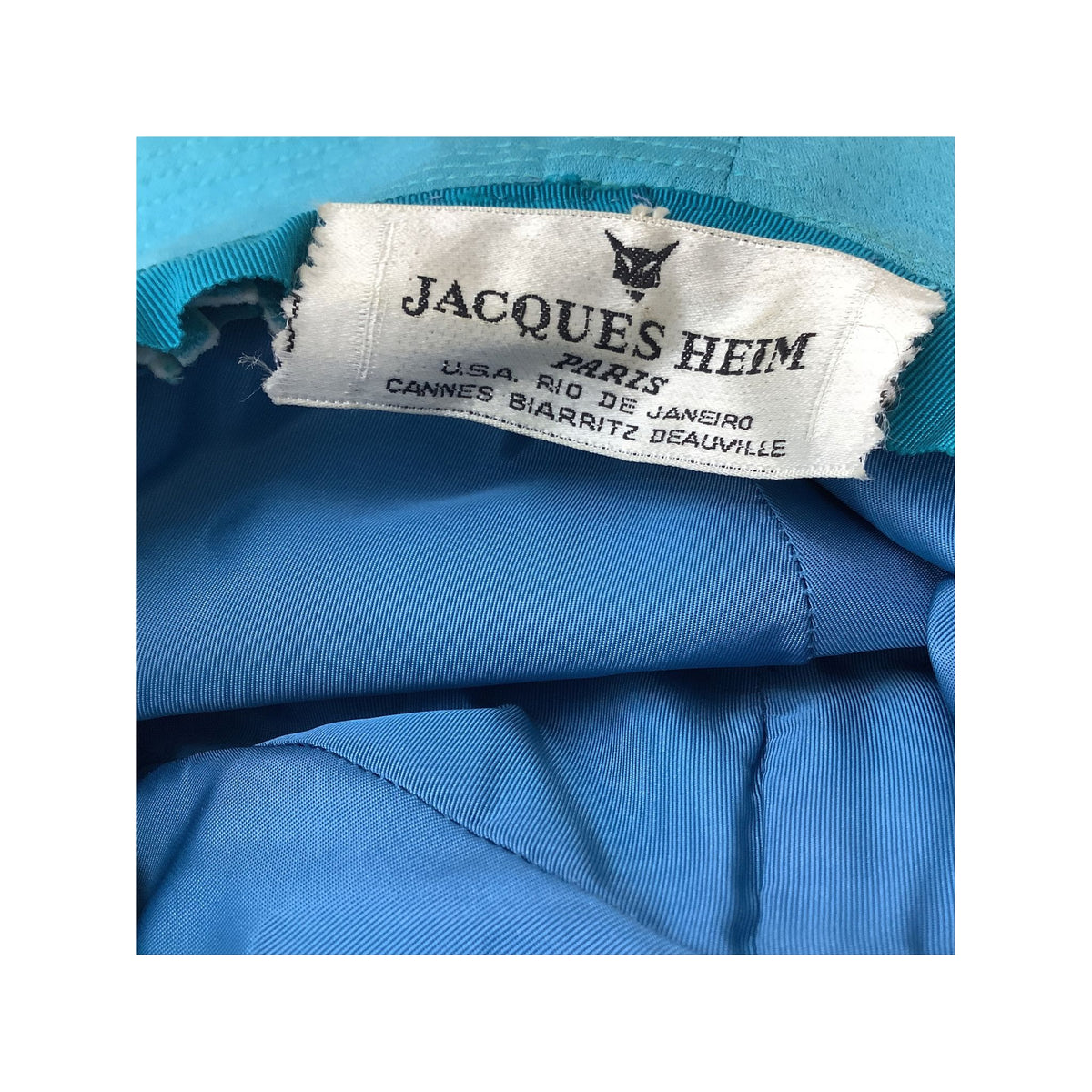Close-up of a blue hat interior showing a white fabric brand label that reads JACQUES HEIM PARIS.
