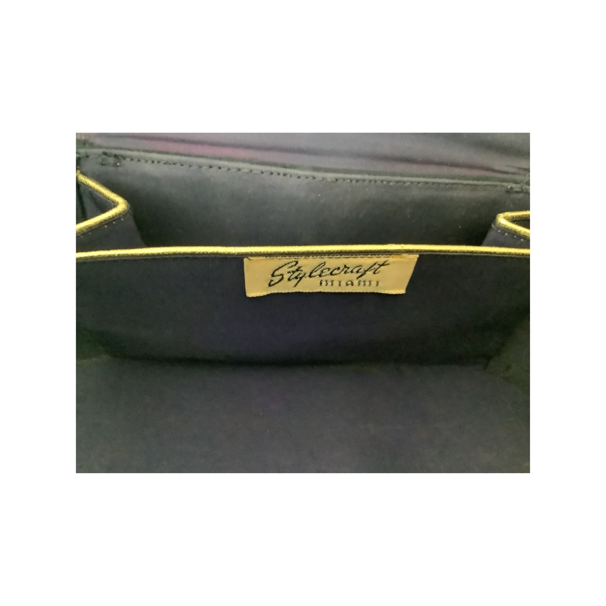 Close-up of a dark navy or black fabric bag interior with yellow piping and a beige brand label reading 'Stylecraft MIAMI'.