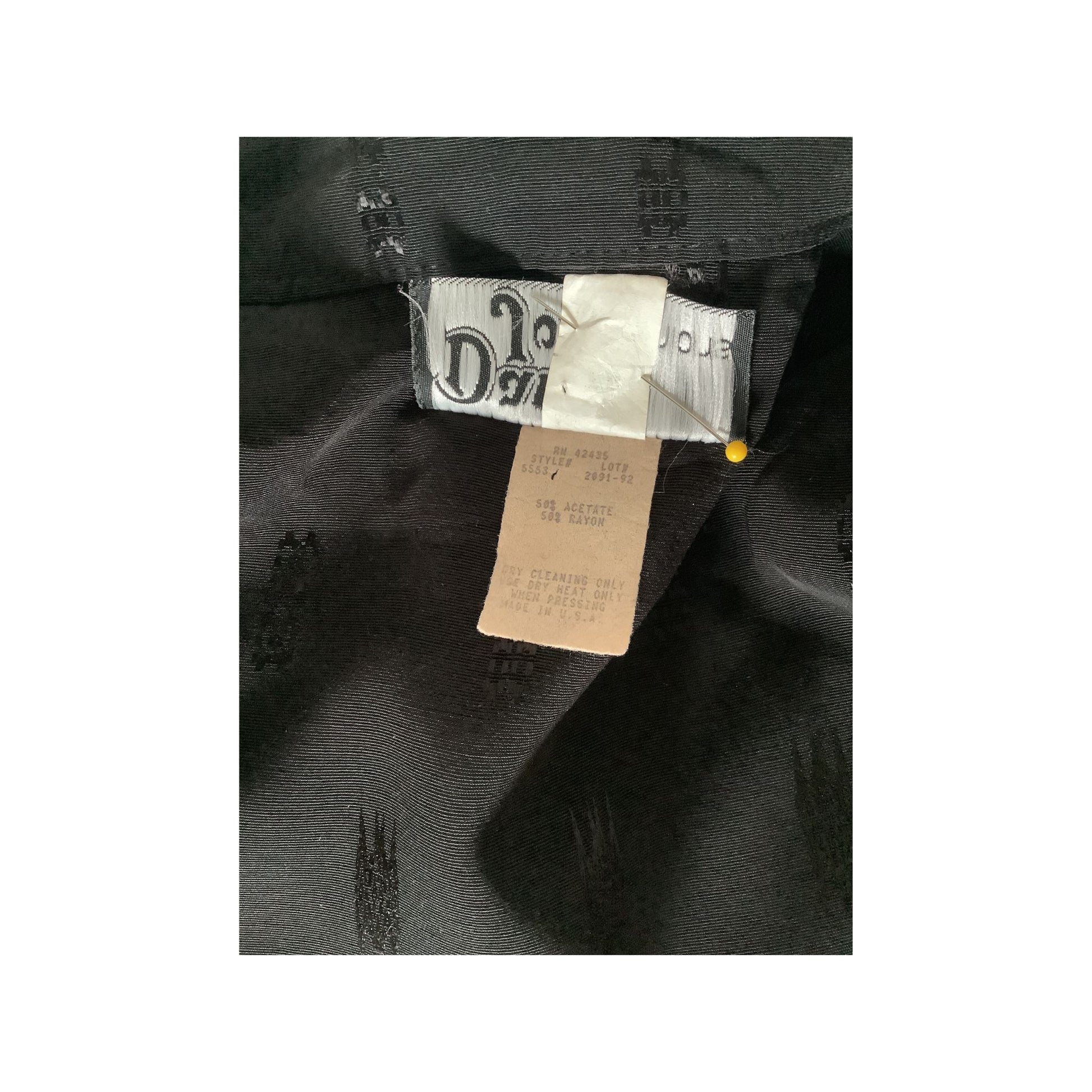 Close-up of a black garment interior showing a sewn-in size label and a beige care tag pinned near the collar.