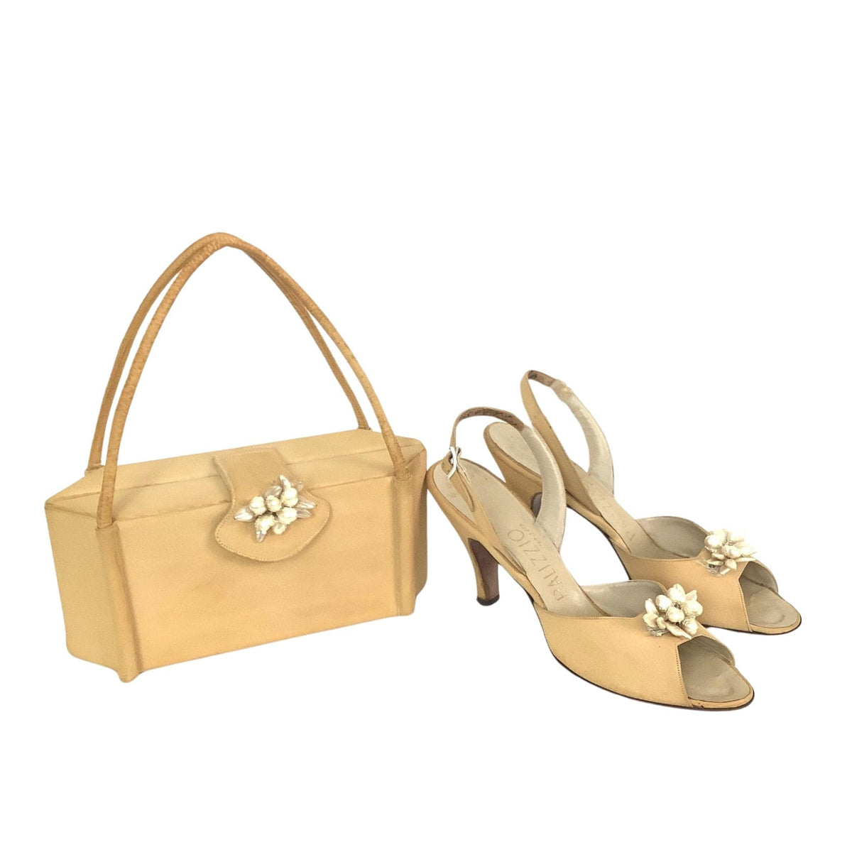 Palizzio coordinated fashion set featuring a structured light beige handbag with a pearl flower embellishment and matching pointed-toe slingback heels with flower accents, displayed on a clean white background.