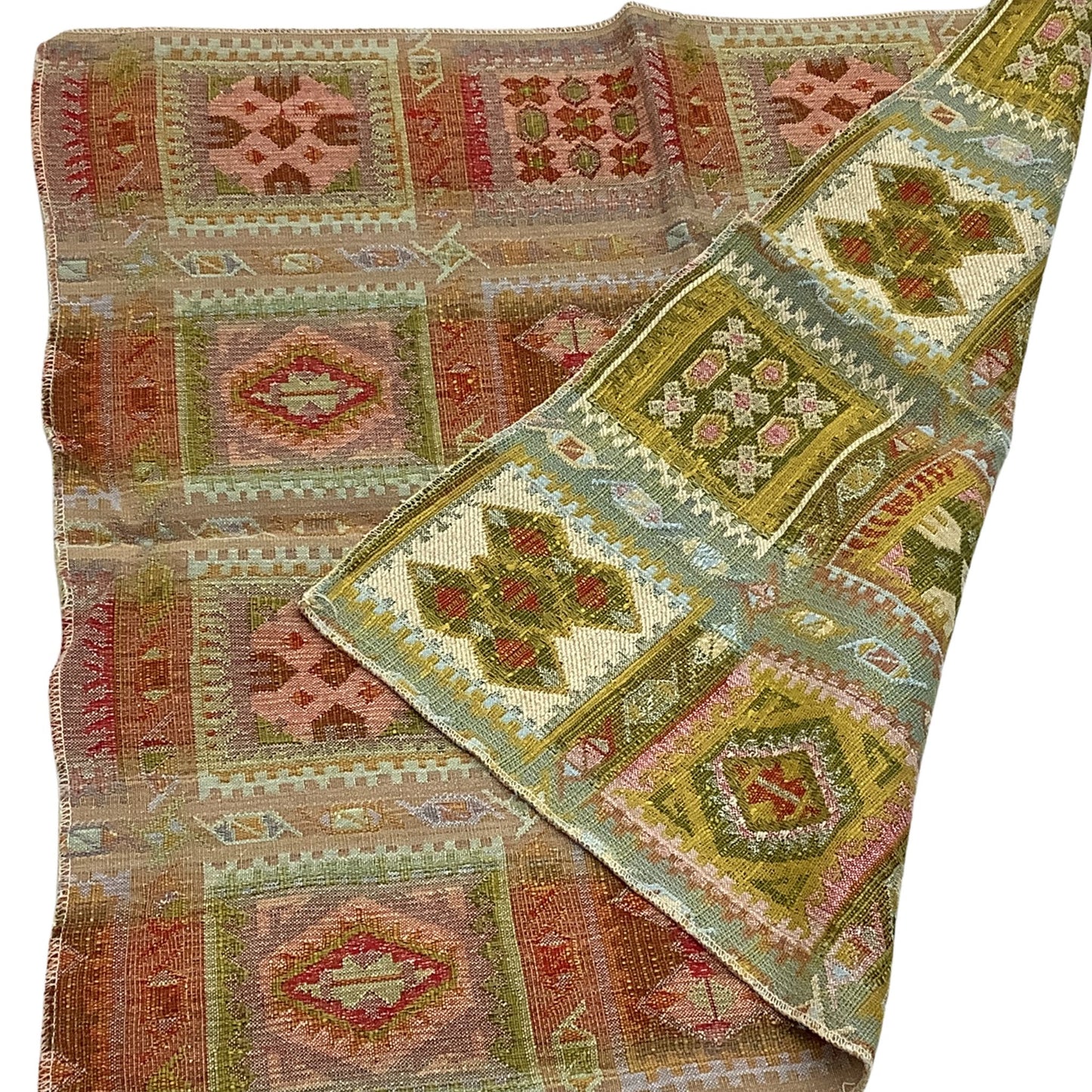 Close-up view of a vintage kilim-stylevintage fabric sample featuring geometric patchwork patterns in muted earthy tones of green, pink, brown, and beige, shown folded diagonally on a white background.