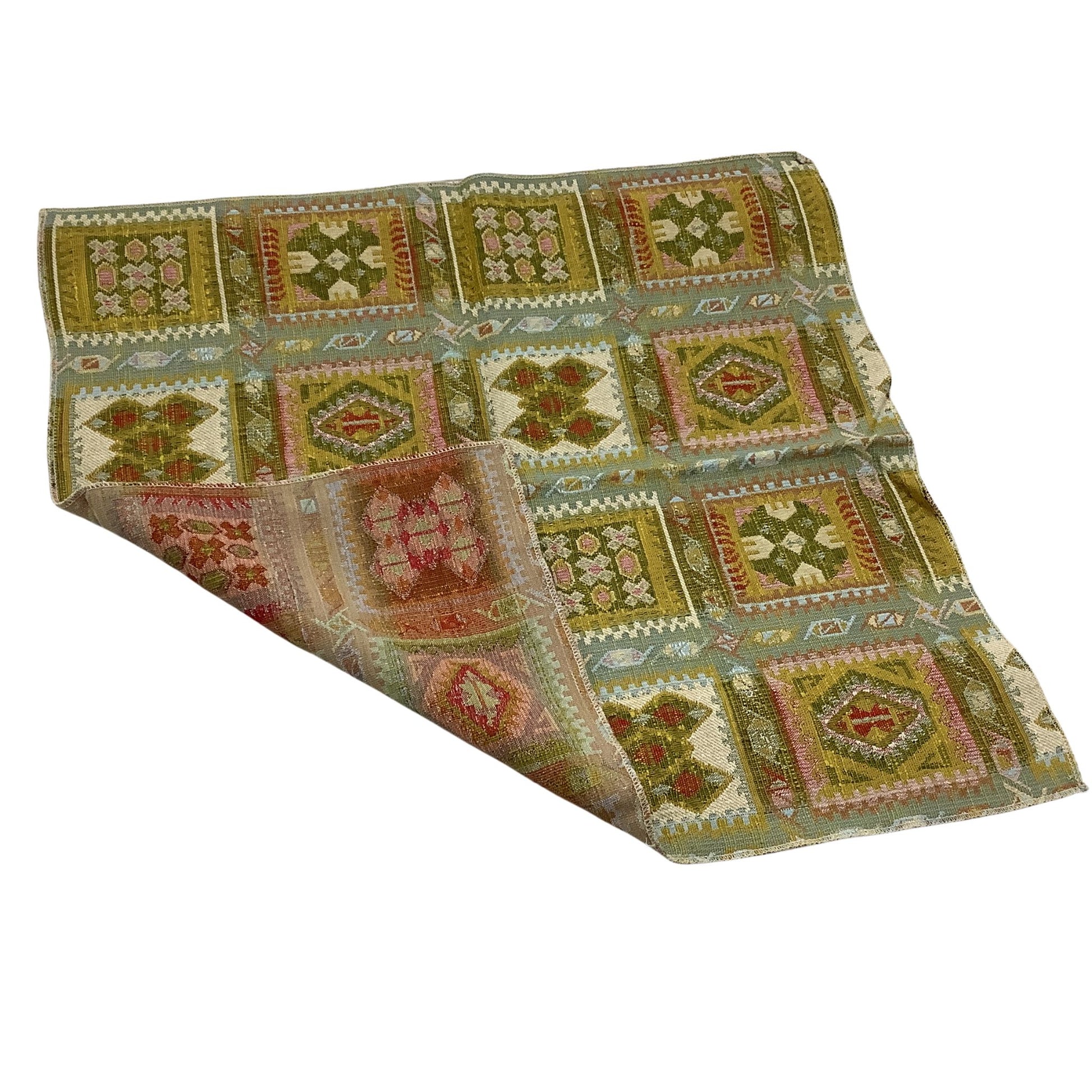 A folded patterned fabric sample, featuring a patchwork design of geometric patterns in muted olive green, beige, pink and rust red.