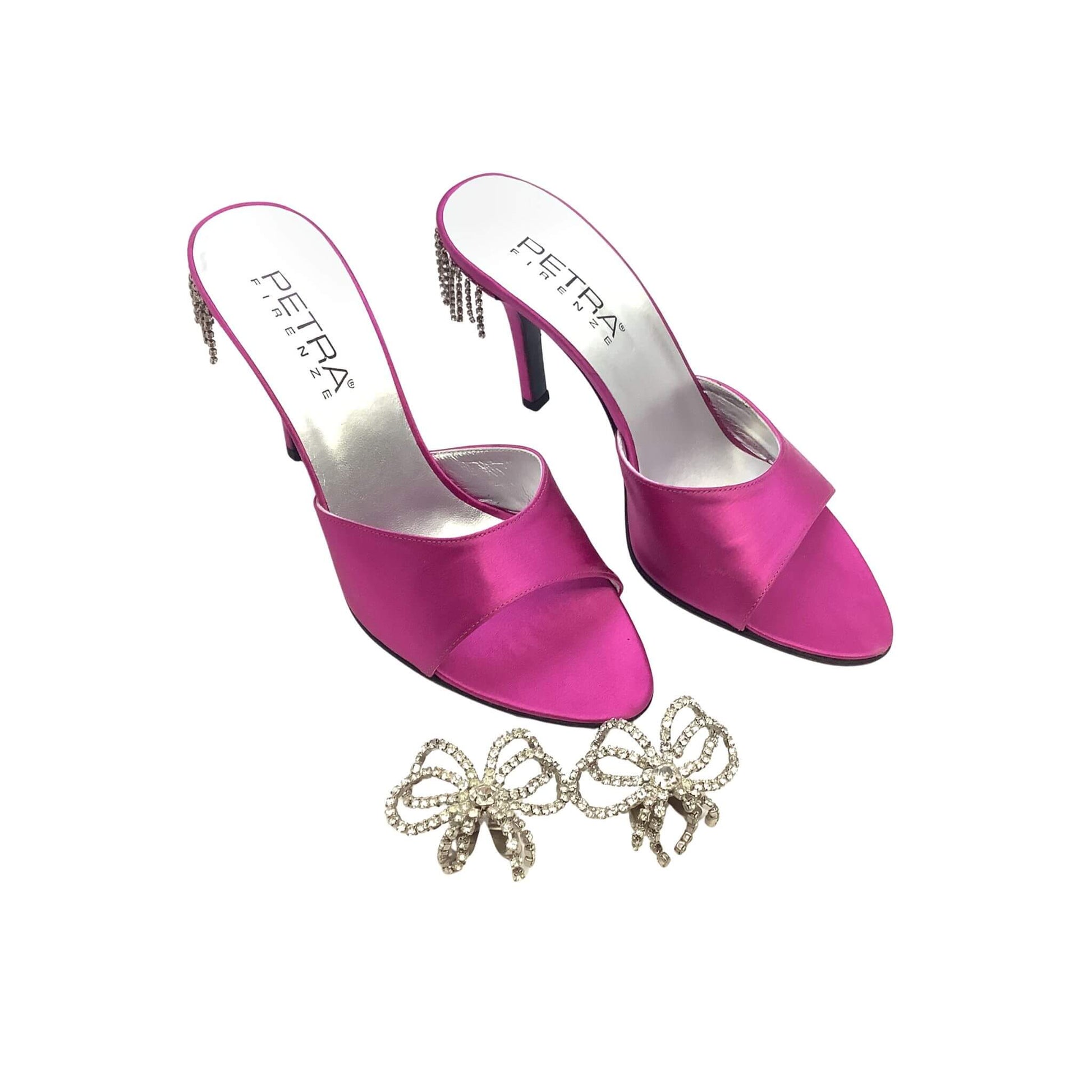 Pink high-heeled shoes with 'Petra' branding and a pair of bow-shaped shoe clips on a white background.