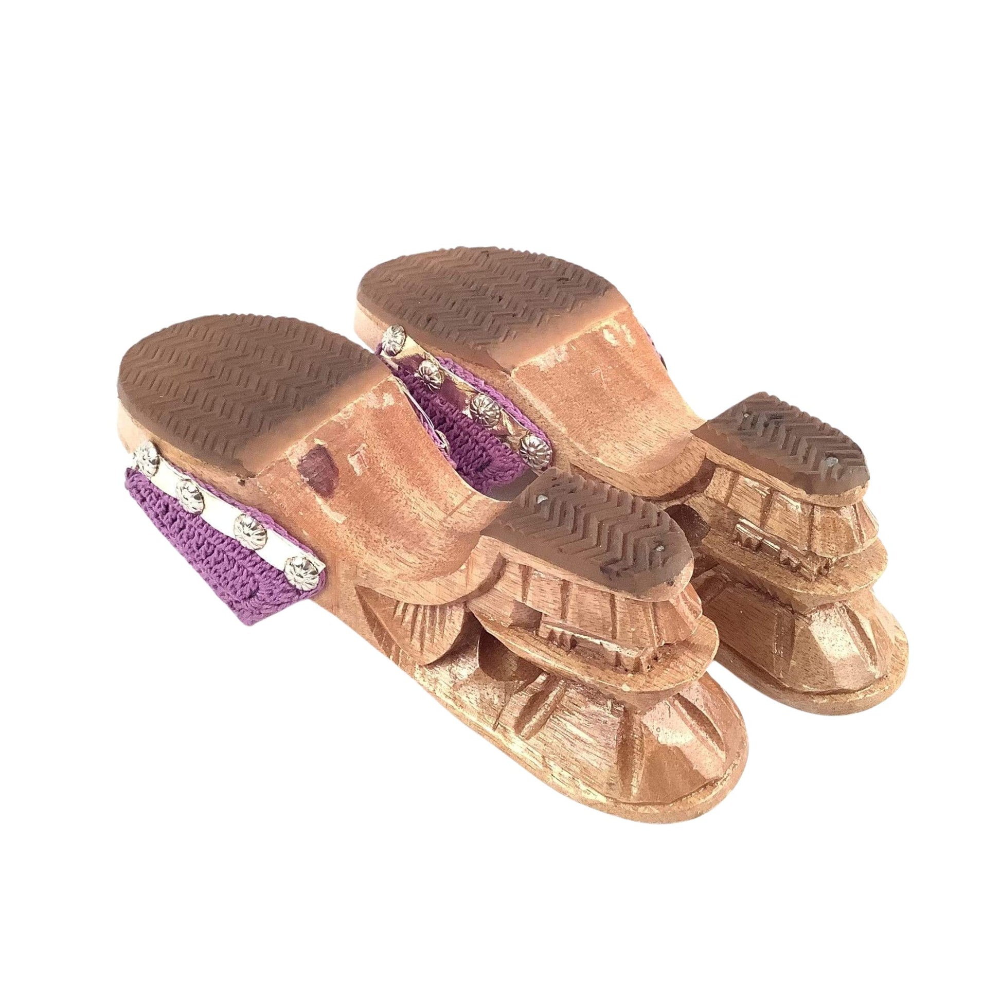 Soles of purple strap sandals with carved wood heels on a white  background