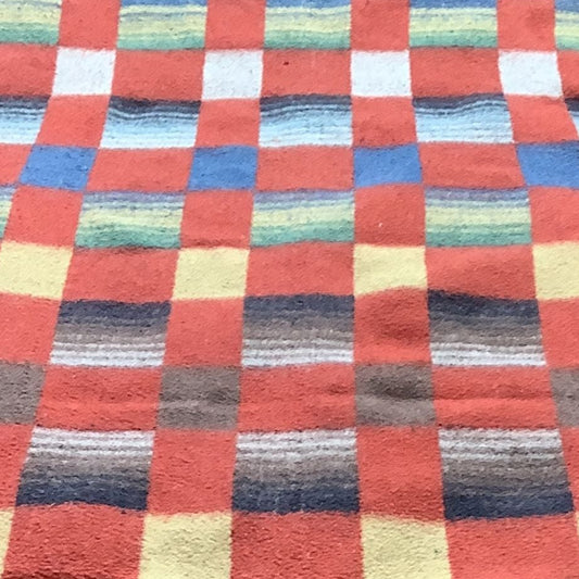 Top view of a vintage 1940s woven  wool blanket in a colorful checkered pattern, featuring alternating blocks of red, blue, green, yellow, and white stripes, shown against a plain white background.
