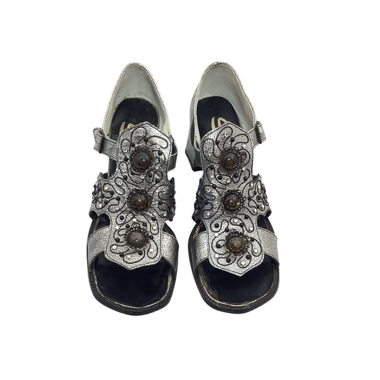 Pair of silver sandals with decorative straps on a white background