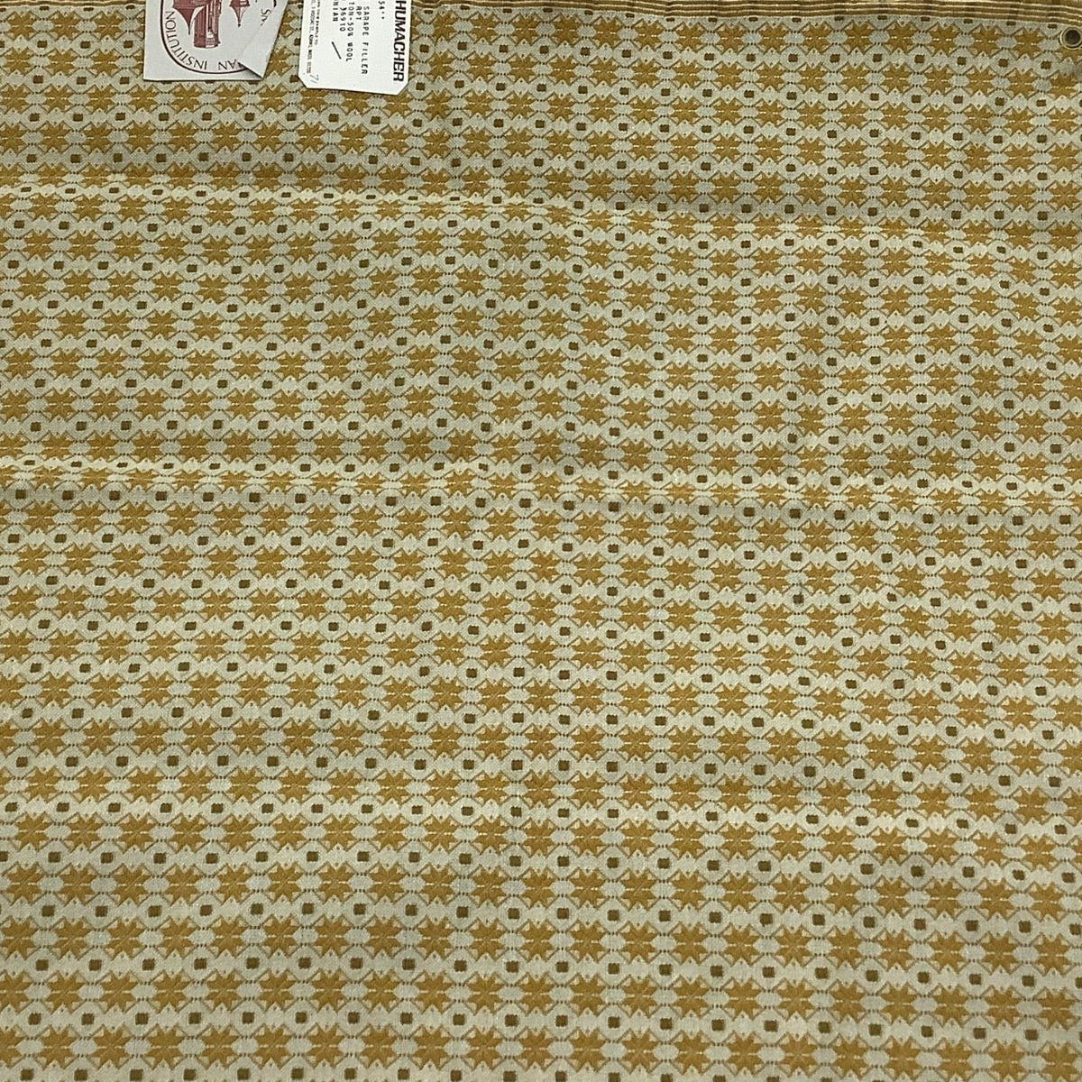 Vintage Schumacher fabric sample featuring a repeating geometric pattern in mustard yellow and off-white. It has frayed edges and two small product tags attached near the top left corner.