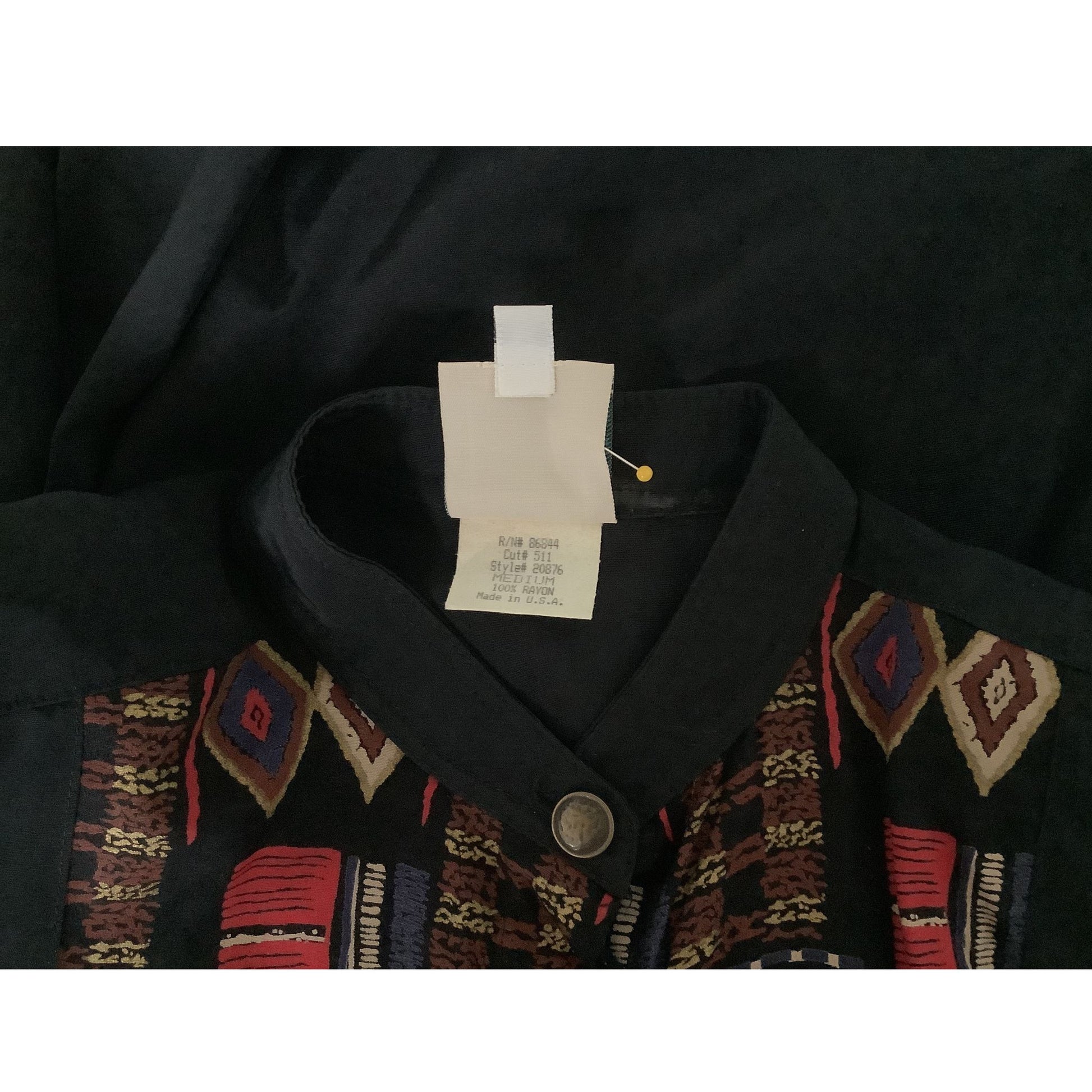 A close-up of a black collared vintage Sherry Holt top with geometric patterned trim in red, beige, and brown, featuring a white size tag.