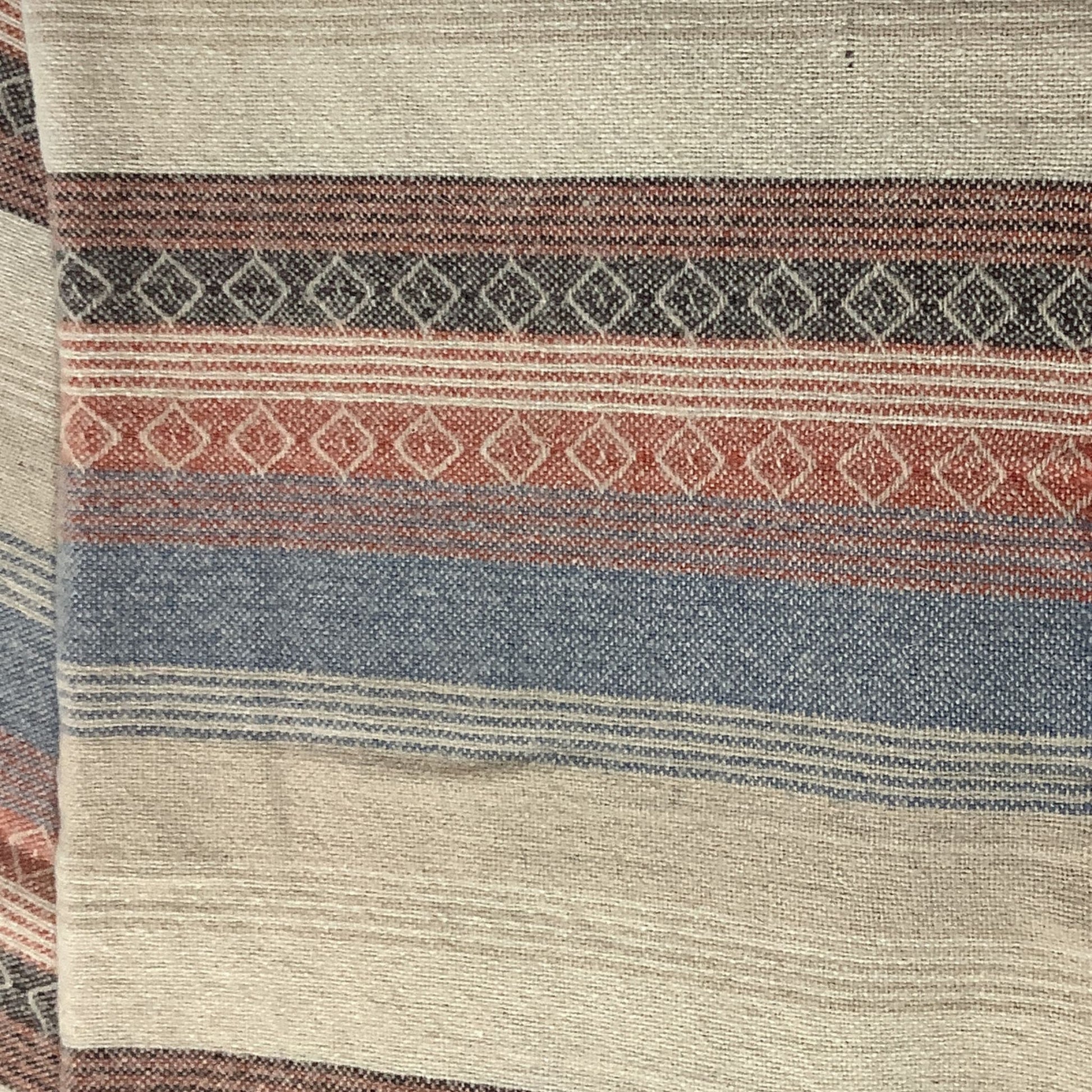 A close-up of a woven textile with horizontal stripes in beige, slate blue, terracotta, and dark brown, featuring stripes and geometric diamond patterns.
