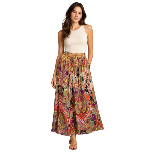 A woman modeling a sleeveless cream top and a long, flowing maxi skirt with a colorful paisley and floral print in orange, red, green, purple, and black, set against a plain white background.