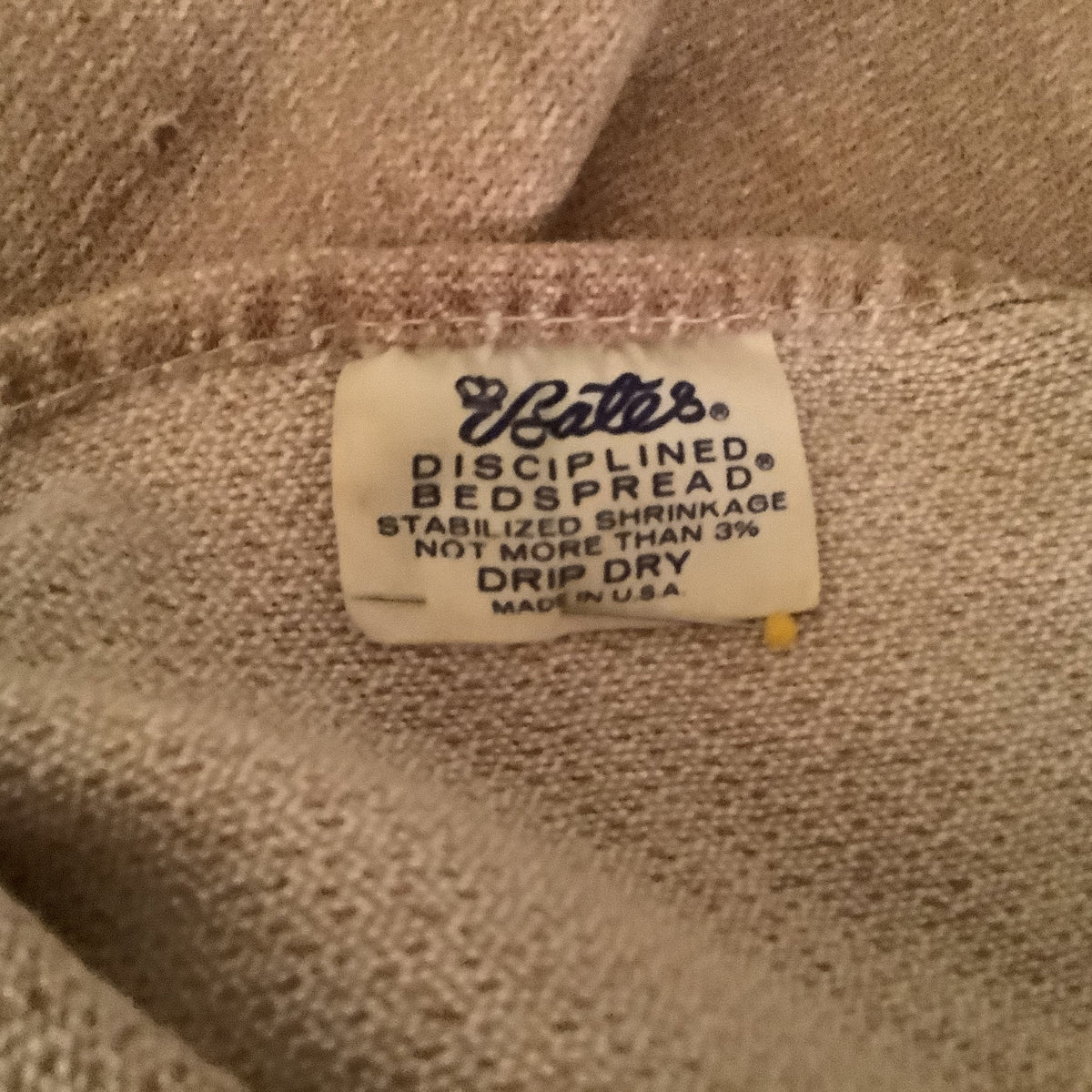 Close-up of a Bates bedspread 'Bates Disciplined Bedspread' sewn onto beige woven bedding.