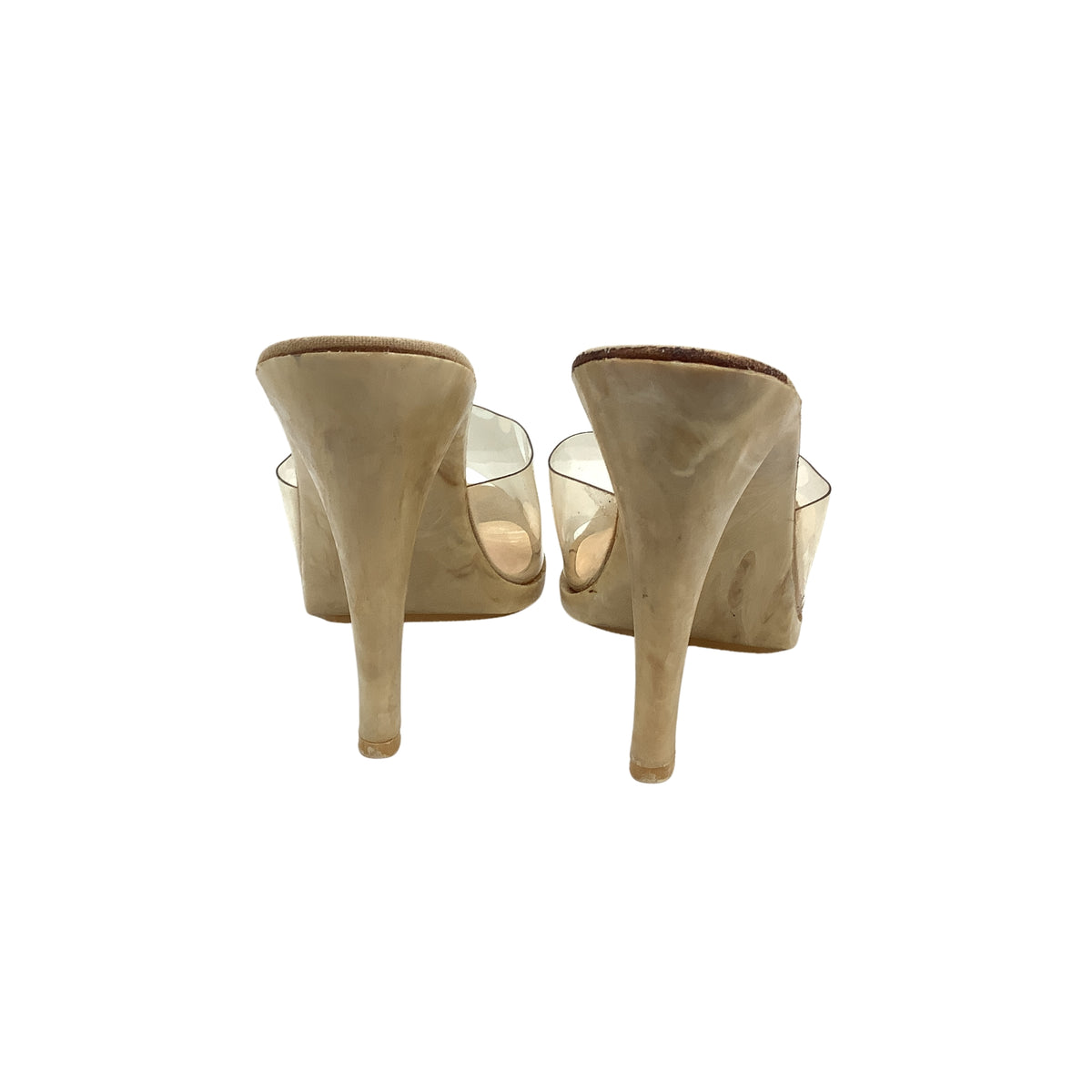 A pair of beige suede high-heeled mule heels with clear plastic uppers, shown from the back.