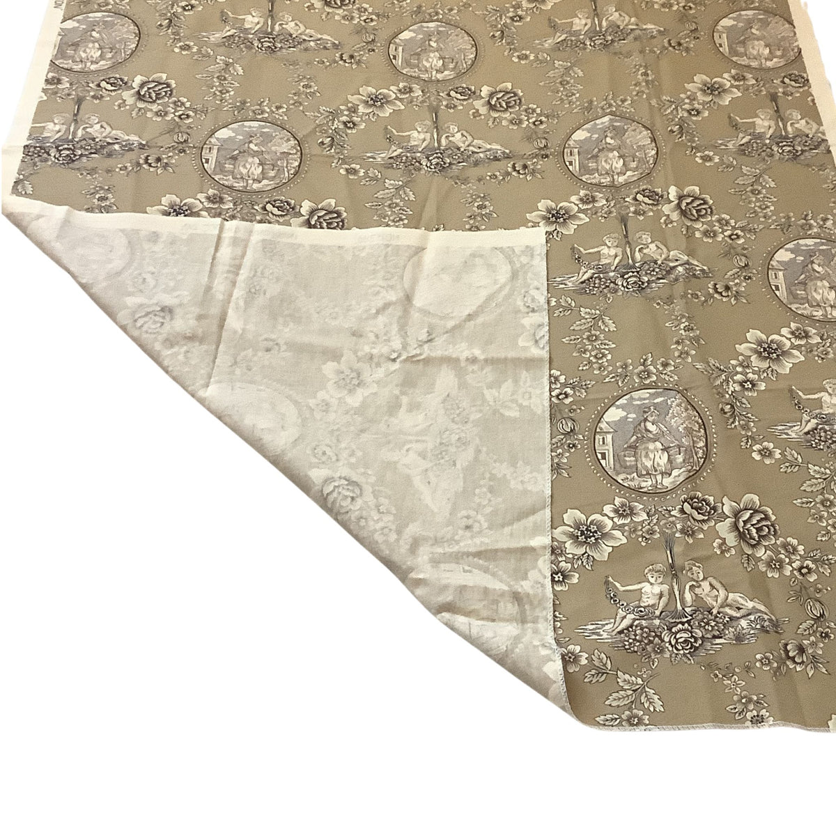 A folded piece of fabric or textile shown on a white background, with one side displaying a beige and taupe toile-style floral and scenic pattern and the other side showing back side in a lighter cream color .