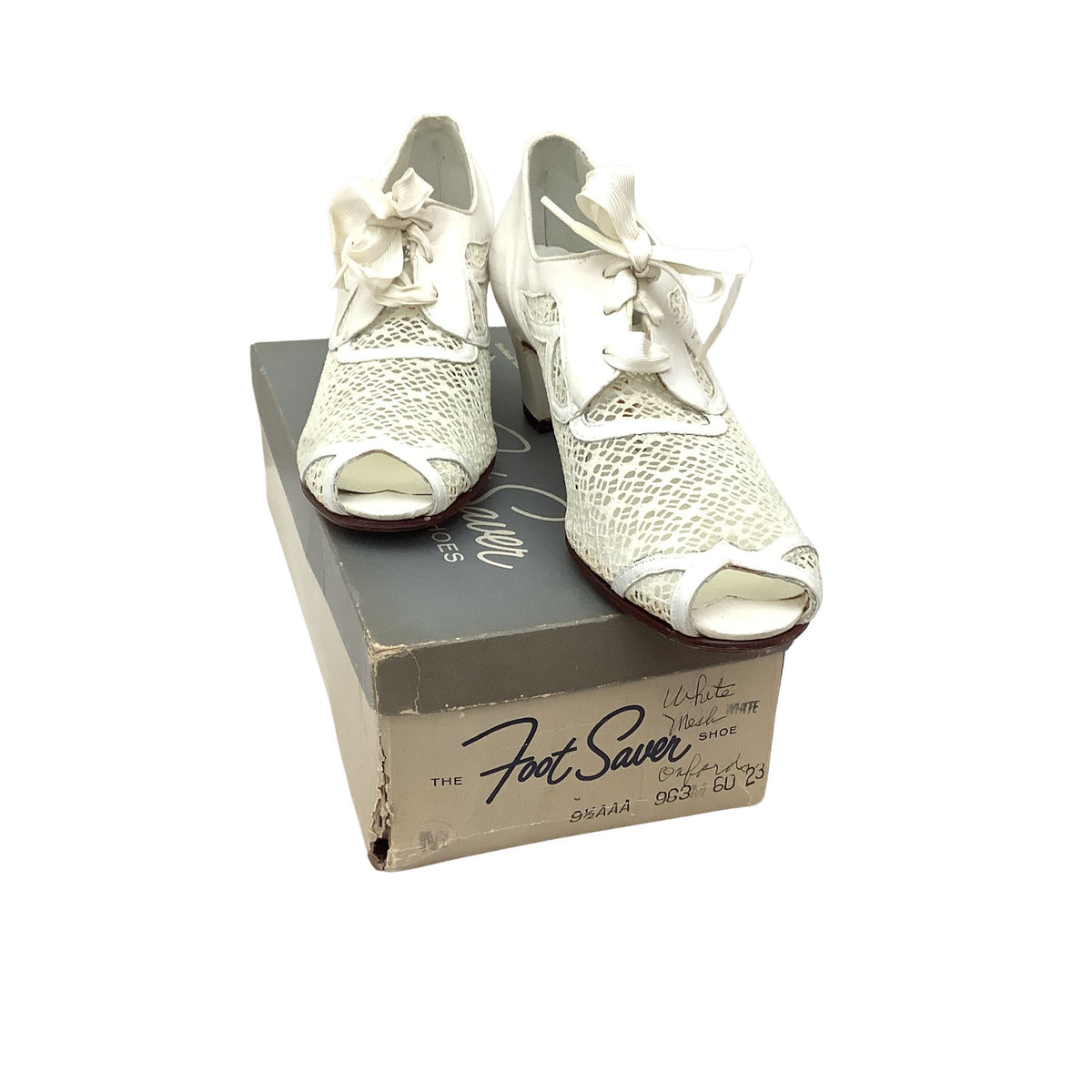 Authentic vintage 1940s pair of white peep-toe heels with textured mesh  uppers and bow details, displayed on top of a vintage gray and beige shoebox. The shoebox features the brand name 'The Foot Saver'.