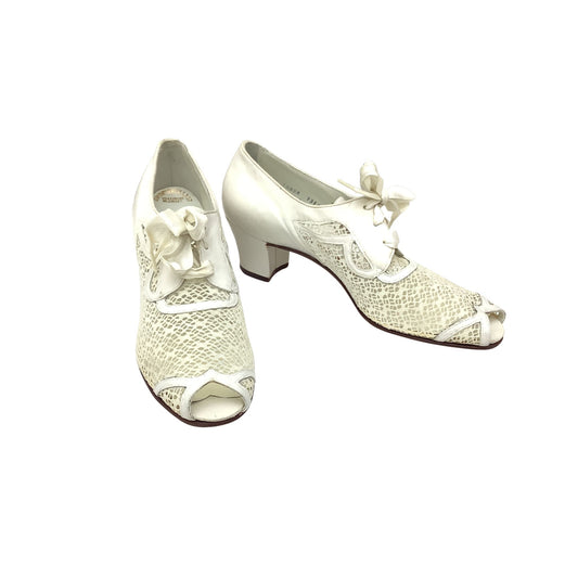 A pair of authentic vintage 1940s mid block-heel oxford shoes in white leather, featuring a textured mesh fabric, peep toe and side panels, laced up with bow details.