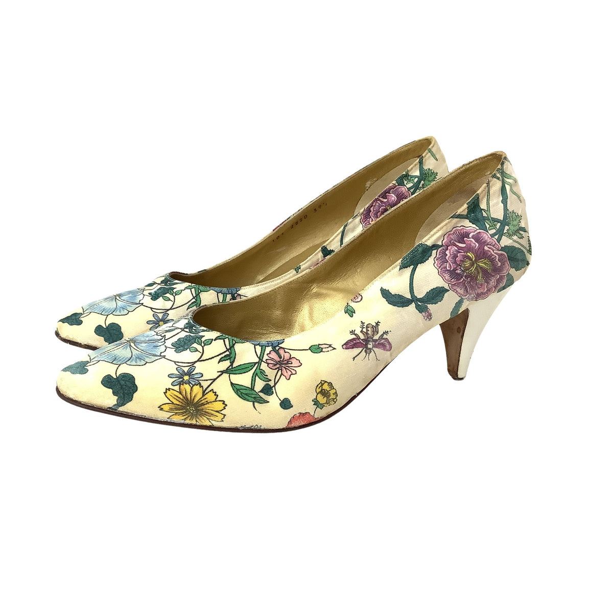 A pair of Gucci mid-height pumps with a cream-colored satin-like fabric covered in a colorful floral print featuring green leaves, yellow and purple flowers, and blue accents.