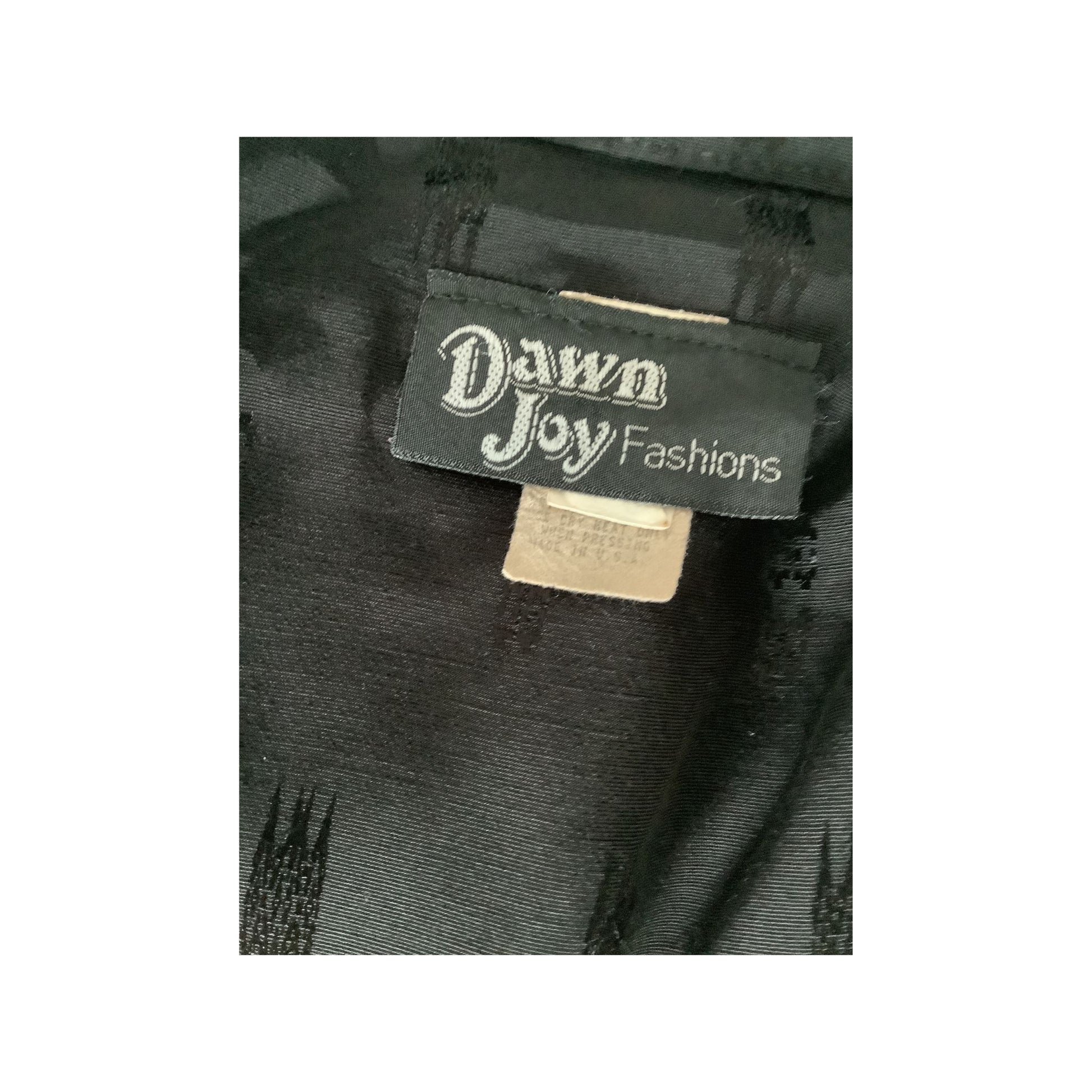 Close-up of a black garment label reading 'Dawn Joy Fashions' on dark textured fabric.