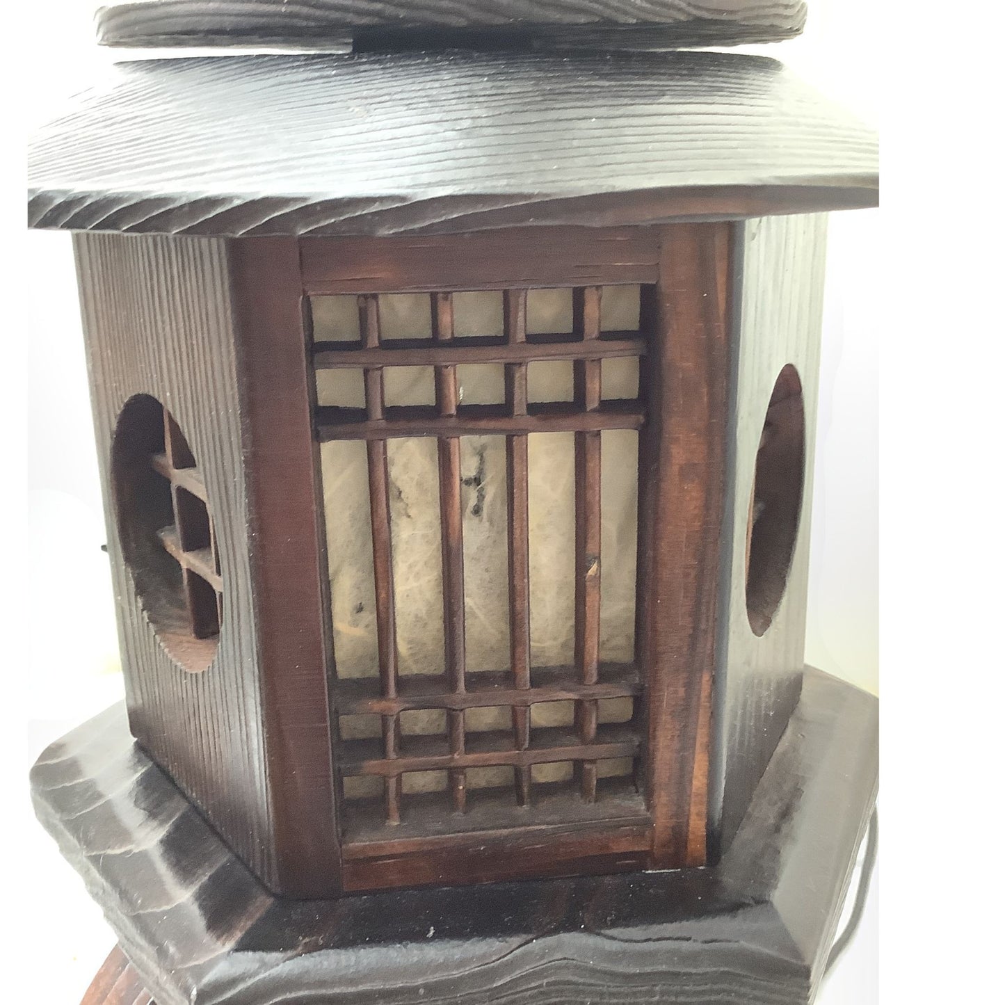 A close-up of a traditional wooden lantern with a dark brown frame, carved lattice window, showing damage to paper insert, set against a plain white background.