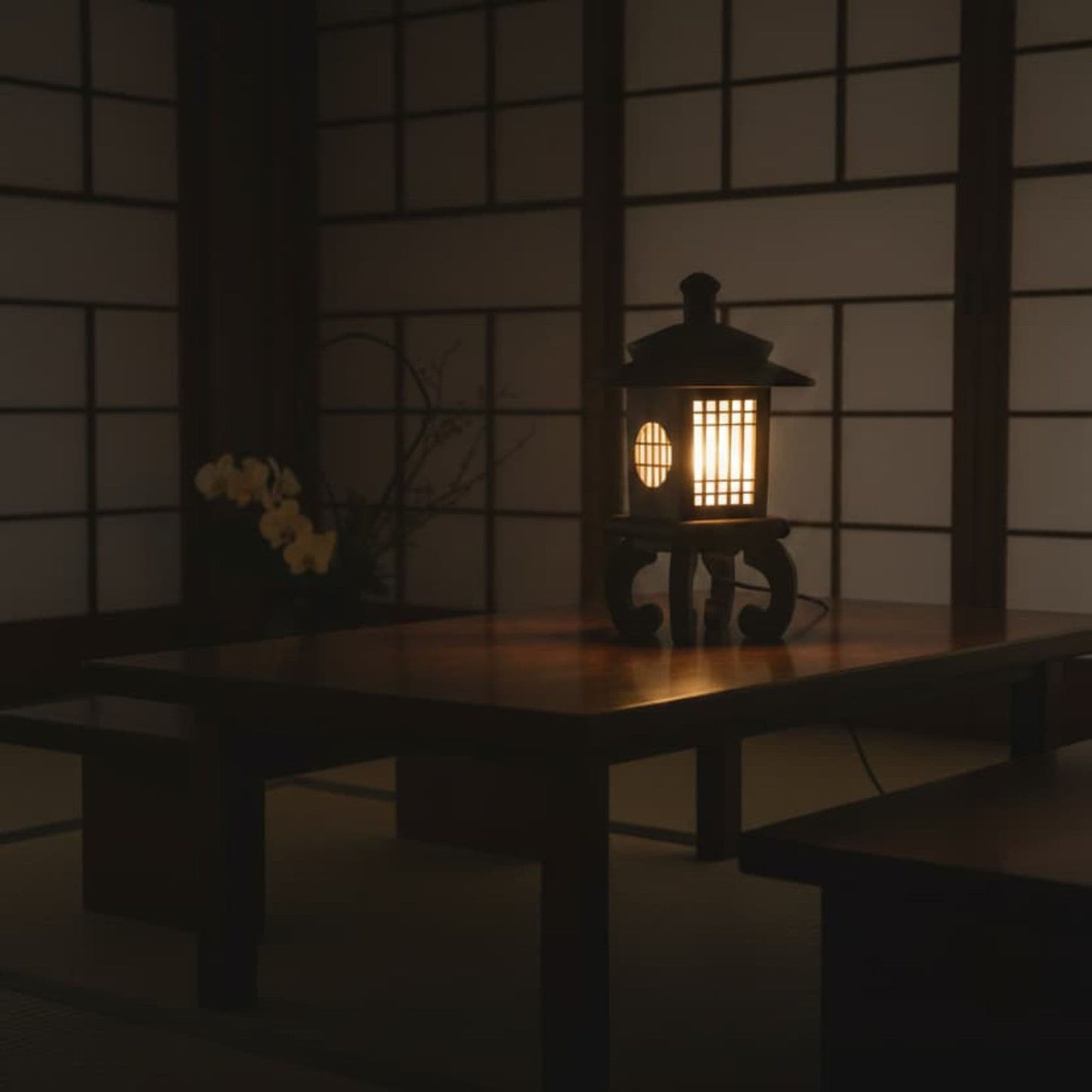 A brown wood Japanese-style lantern with a warm glowing light inside, placed on a low wooden table in a traditional room with shoji screens.