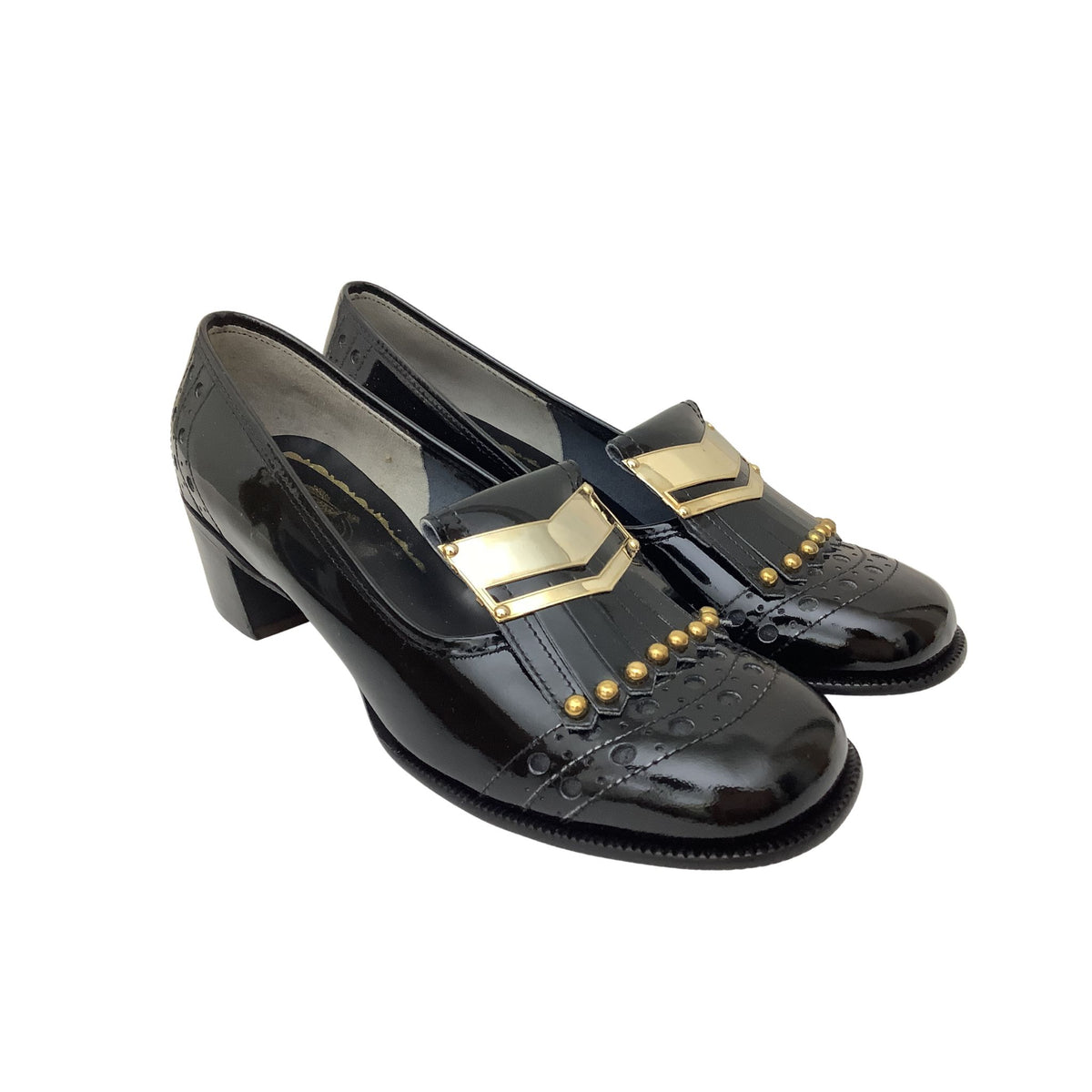 A pair of vintage black patent leather loafers with a low block heel, embossed pattern on the toe, and gold chevron and stud accents on the vamp, shown against a plain white background.