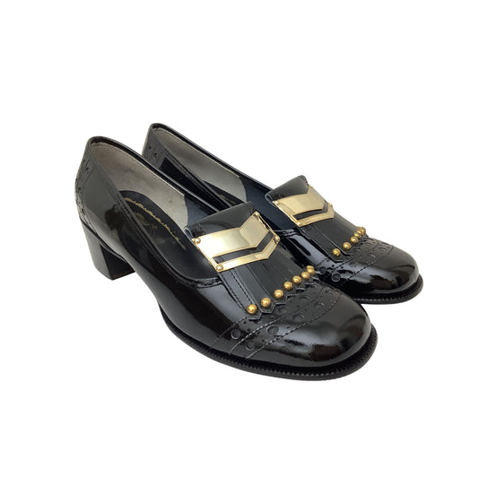 A pair of vintage black patent leather loafers with a low block heel, embossed pattern on the toe, and gold chevron and stud accents on the vamp, shown against a plain white background.