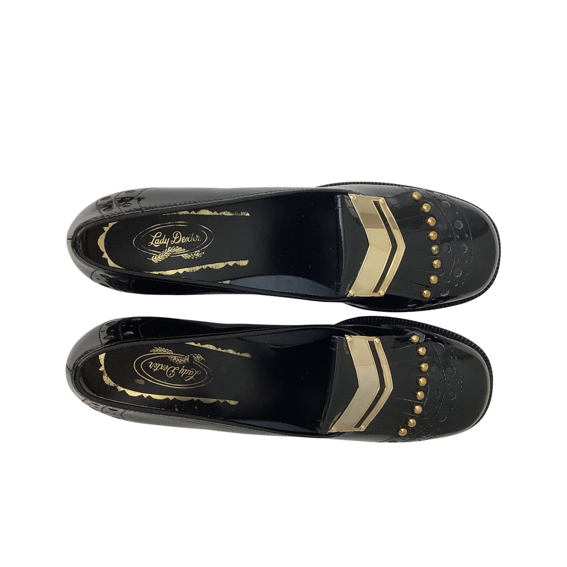 A pair of black patent leather loafers shown from a top-down view, featuring gold chevron stripes, gold studs, and a gold-embossed logo on the insole by the brand 'Lady Dexter'.