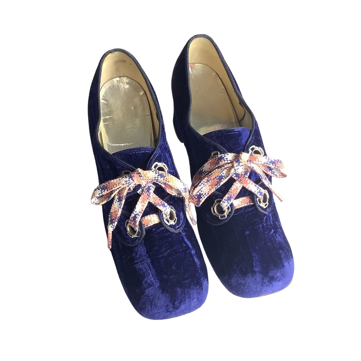Pair of blue velvet shoes with decorative pink, and white laces on a white background